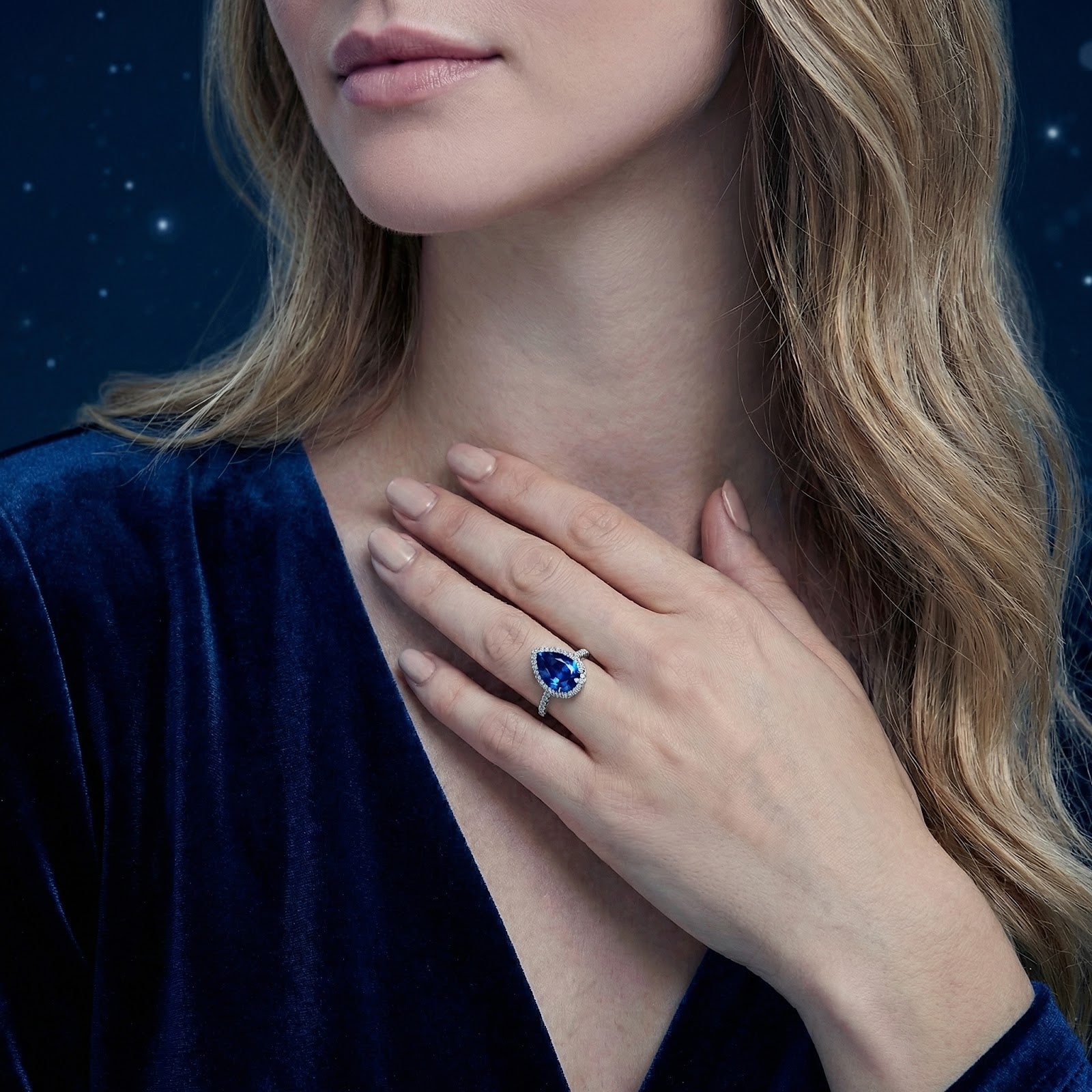 Model wearing a pear cut simulated sapphire halo ring in S925 sterling silver with a blue velvet dress.
