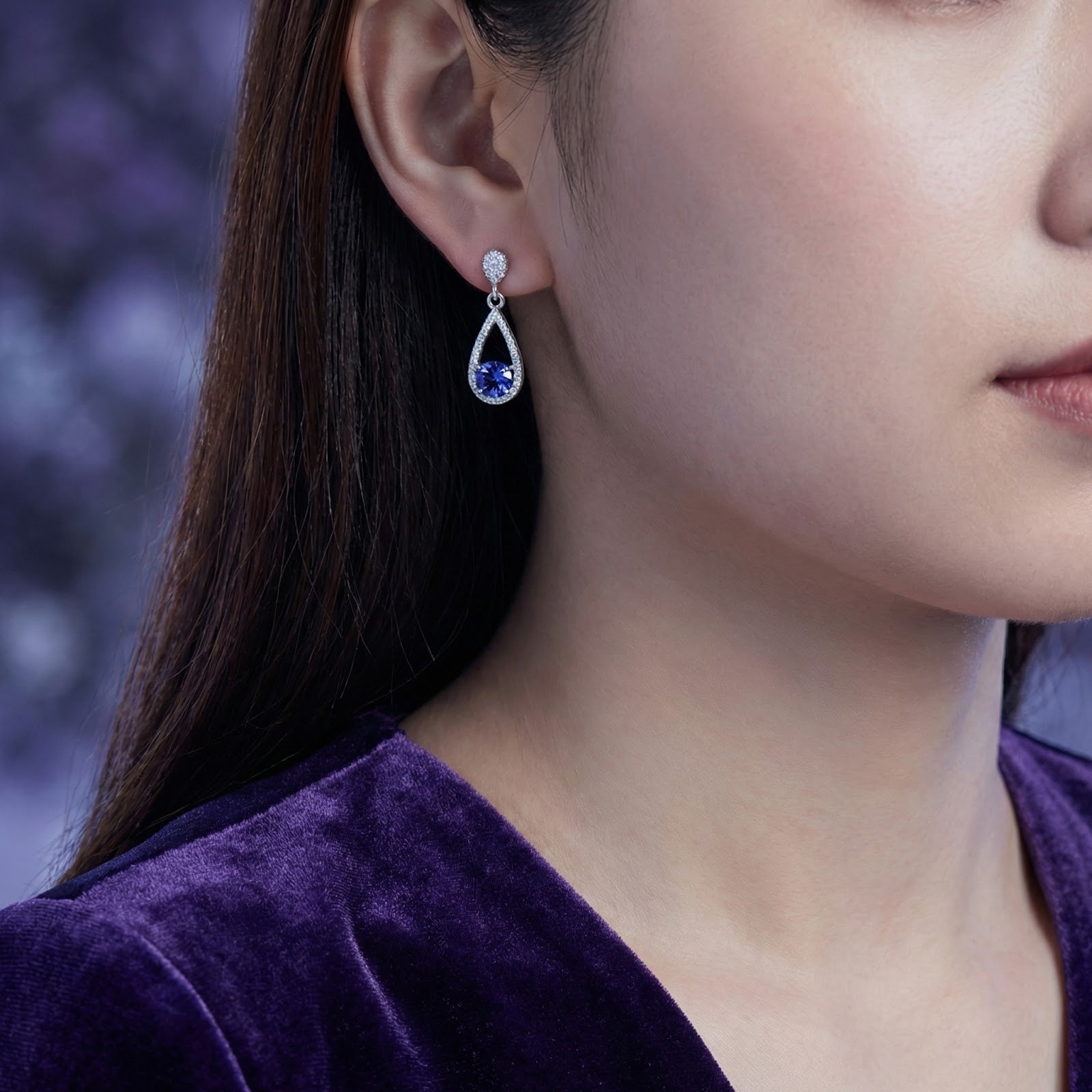 Woman wearing a sterling silver teardrop earring with a round blue simulated tanzanite stone.