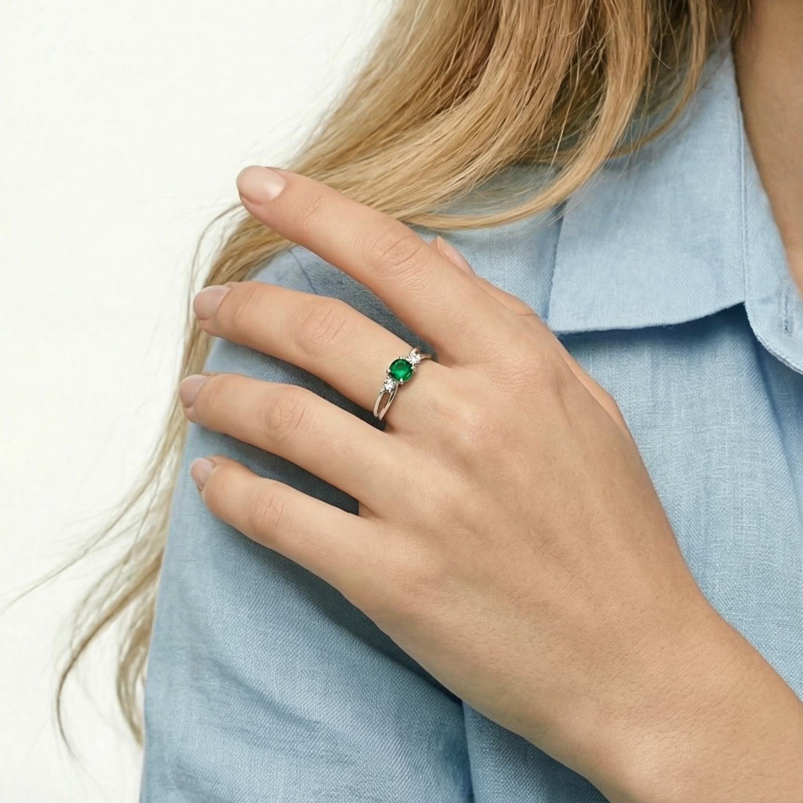 Sterling silver bypass ring with a round green simulated emerald worn on a woman's hand.