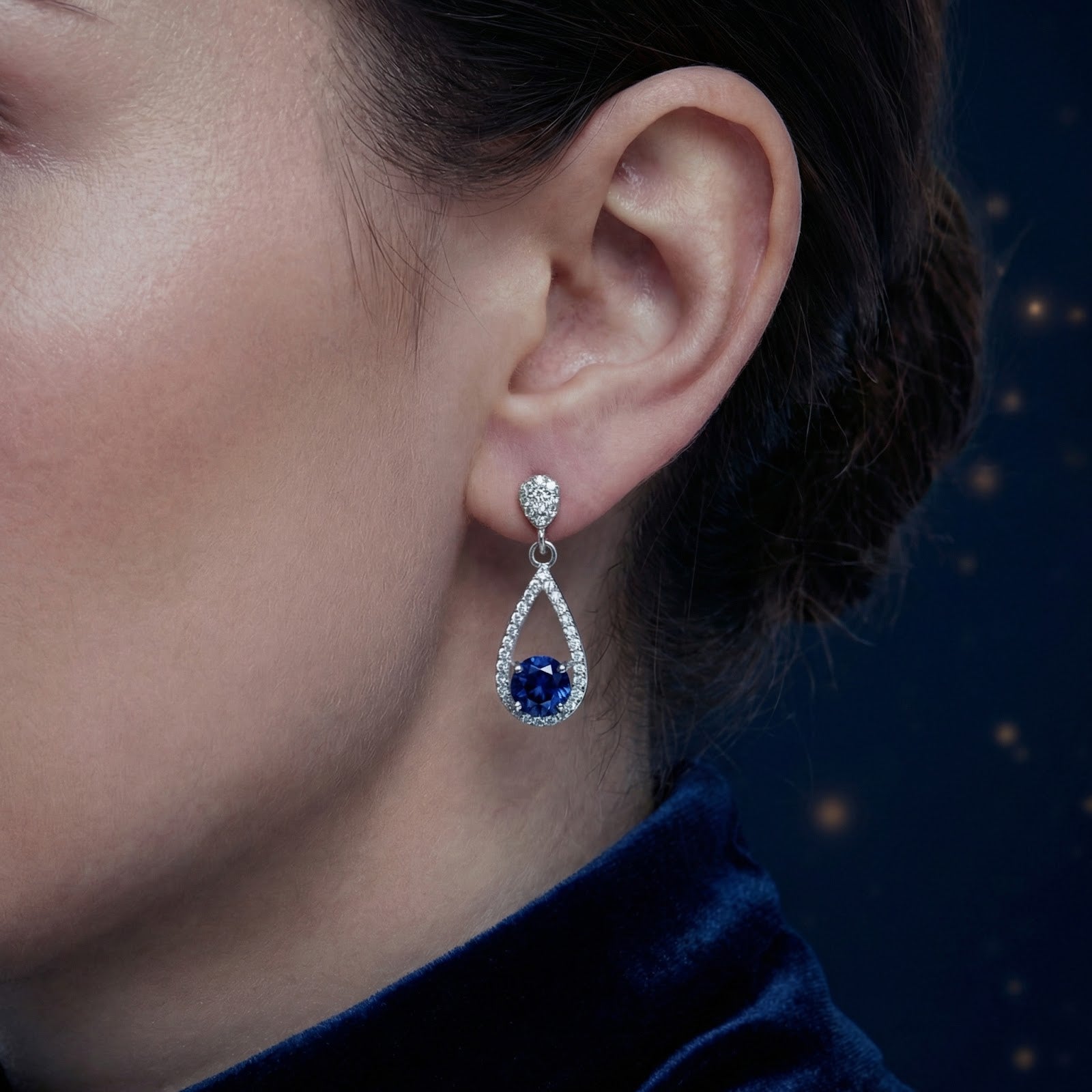 Side view of a sterling silver teardrop earring with a round blue sapphire worn on a model's ear.