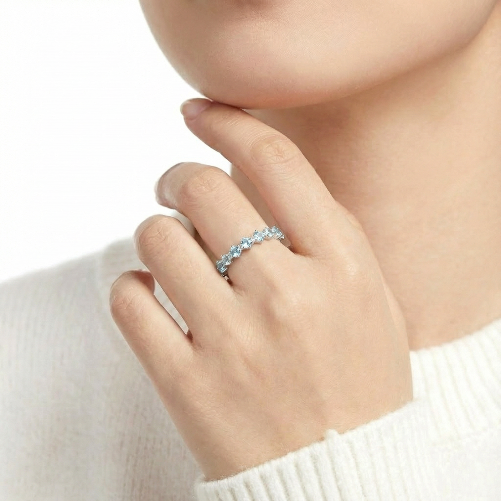 Close-up of a hand wearing a silver ring set with round cut light blue simulated aquamarine gemstones.
