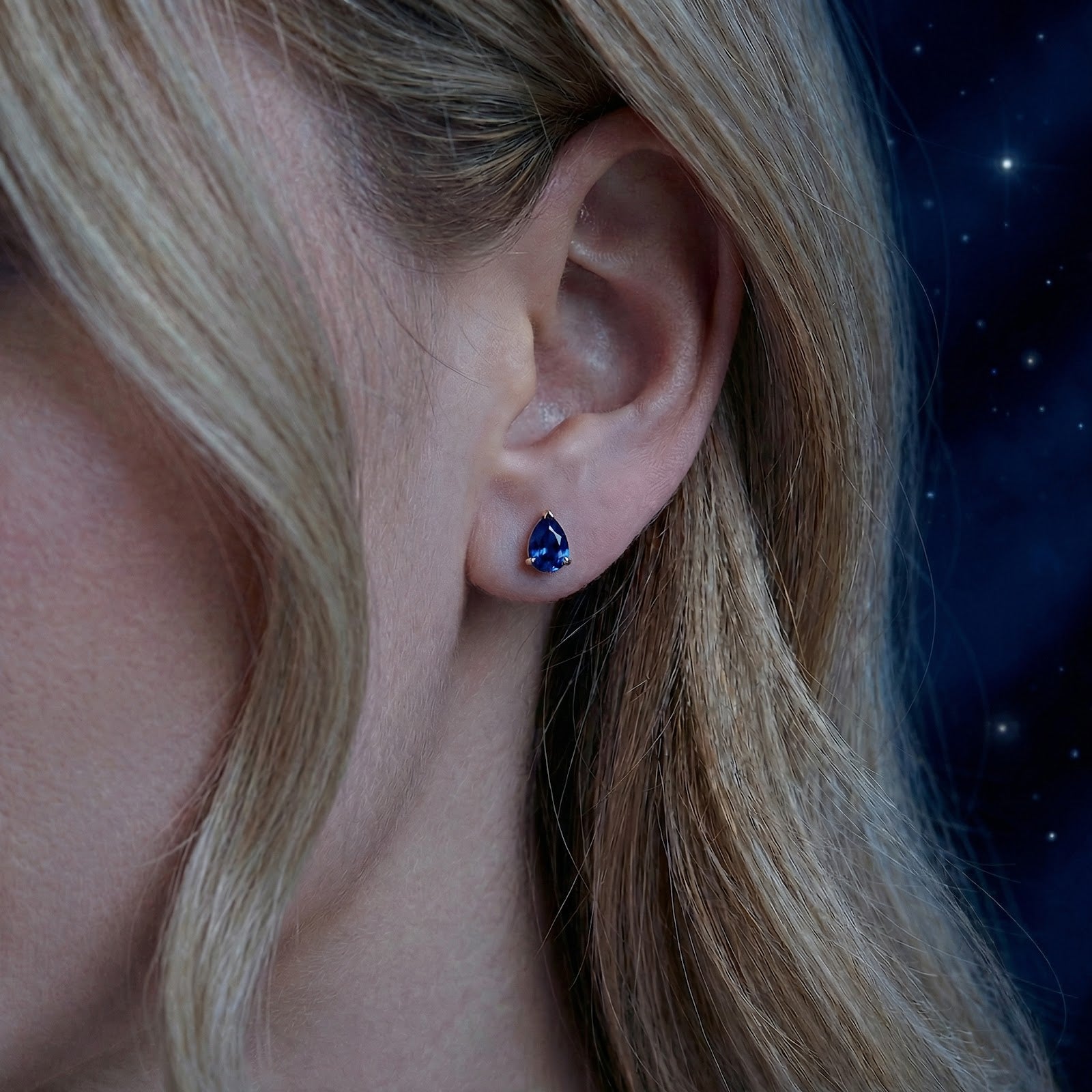 Close-up of a pear-cut simulated sapphire stud earring in 18K gold vermeil on a model's ear.
