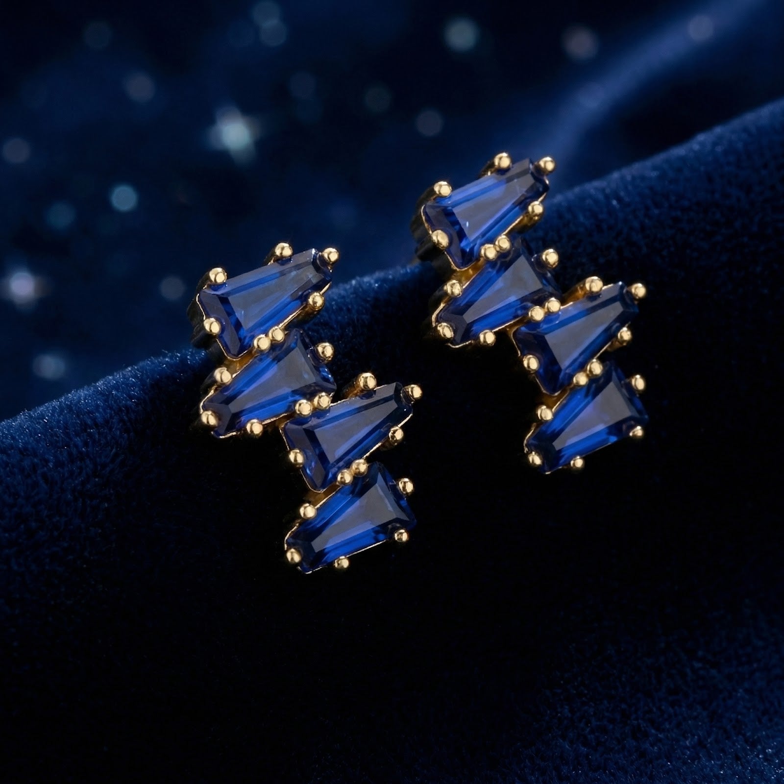 Angled view of Vesperis 18K gold vermeil cluster earrings with blue simulated sapphires on navy velvet.