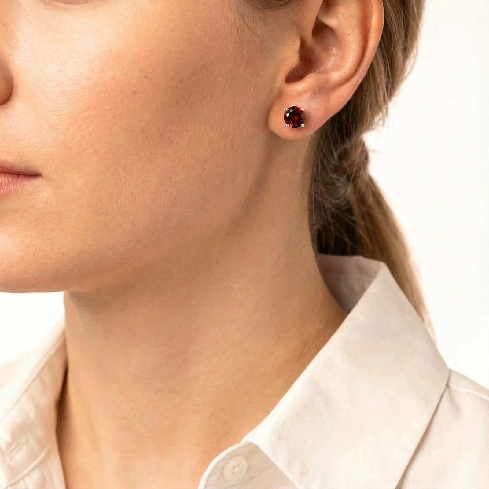 Woman wearing a round cut simulated garnet and sterling silver stud earring from the Thalara collection.
