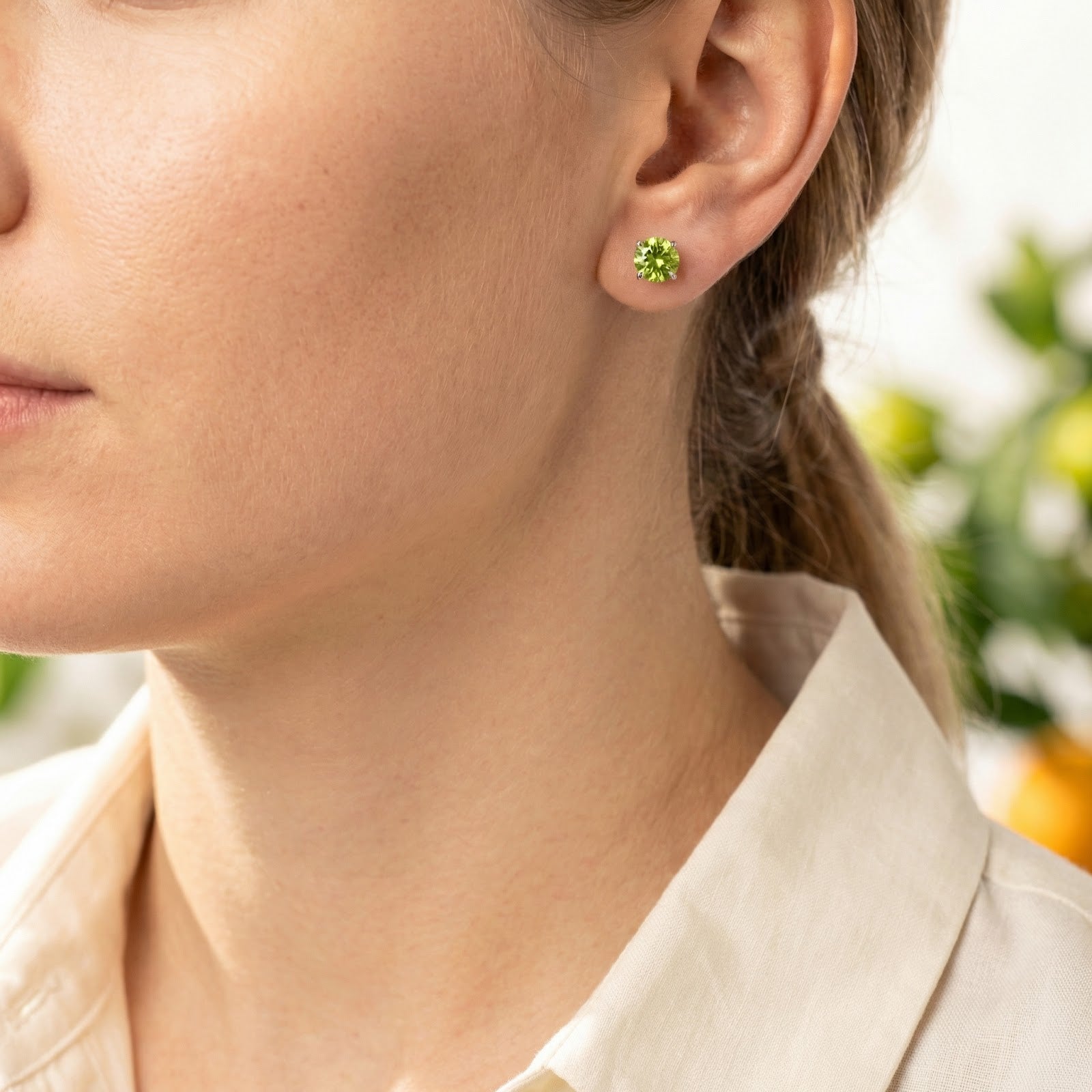 Side profile of a woman wearing the Olyris sterling silver stud earrings with vibrant green simulated peridot.