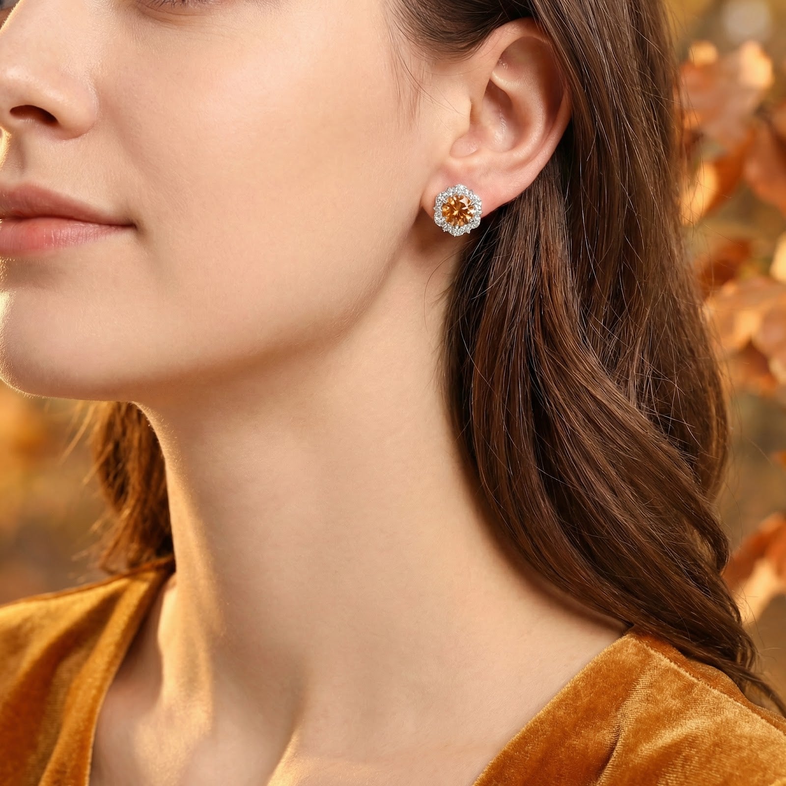 Woman wearing a sterling silver halo stud earring with a round simulated topaz, styled with a gold velvet top.
