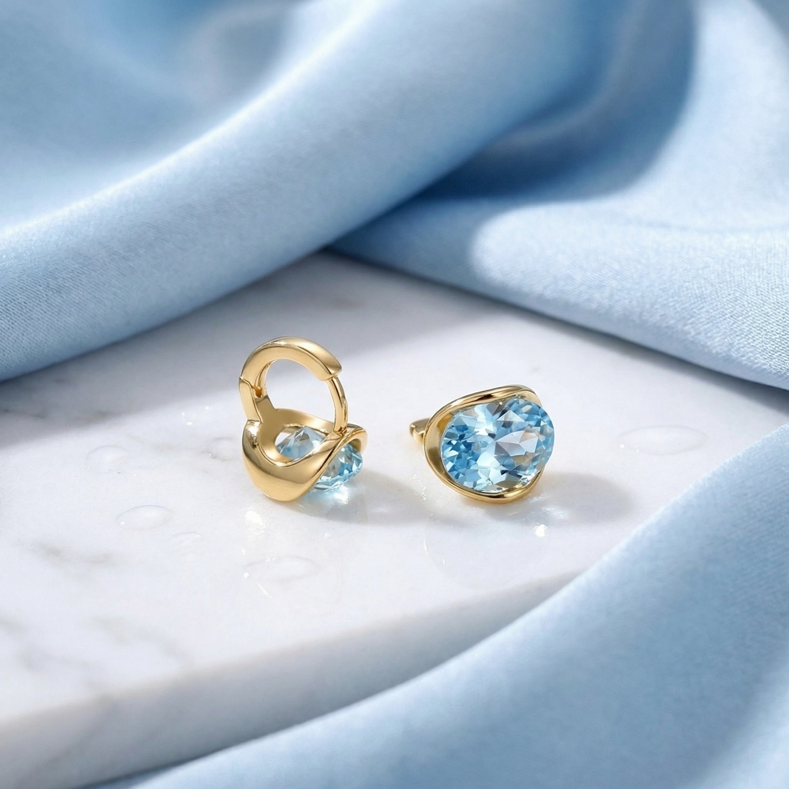 Detail of 18K gold vermeil huggie earrings showing the hinge clasp and oval-cut simulated aquamarine stones.