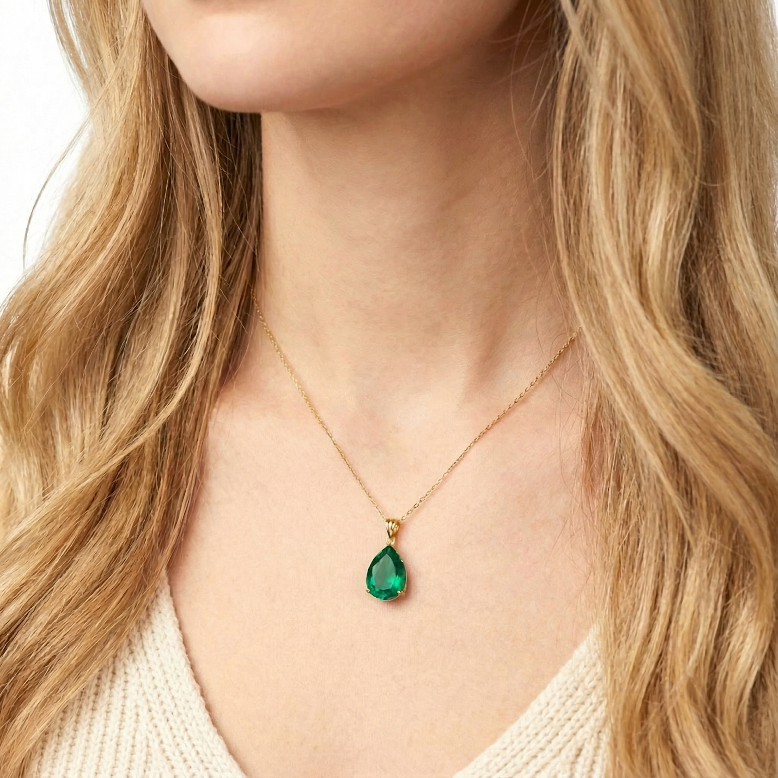 Close-up of a woman wearing a gold vermeil pear-cut simulated emerald necklace against a white knit sweater.