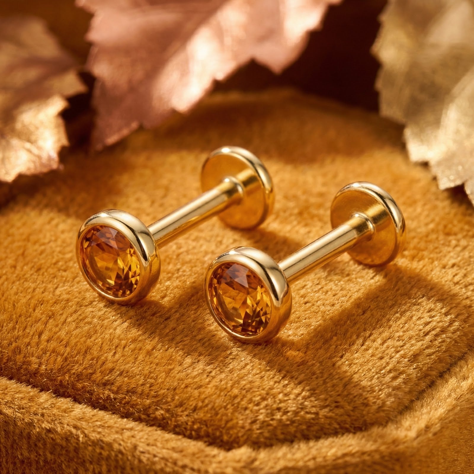 Side view of 18K gold vermeil flat back studs with round-cut honey topaz on velvet with autumn leaves.