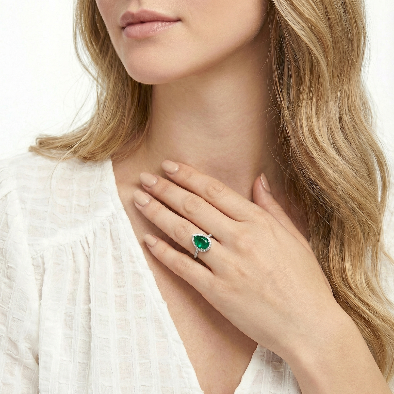 Model wearing a pear-shaped simulated emerald halo ring in silver, showing the jewelry's scale and rich green color.
