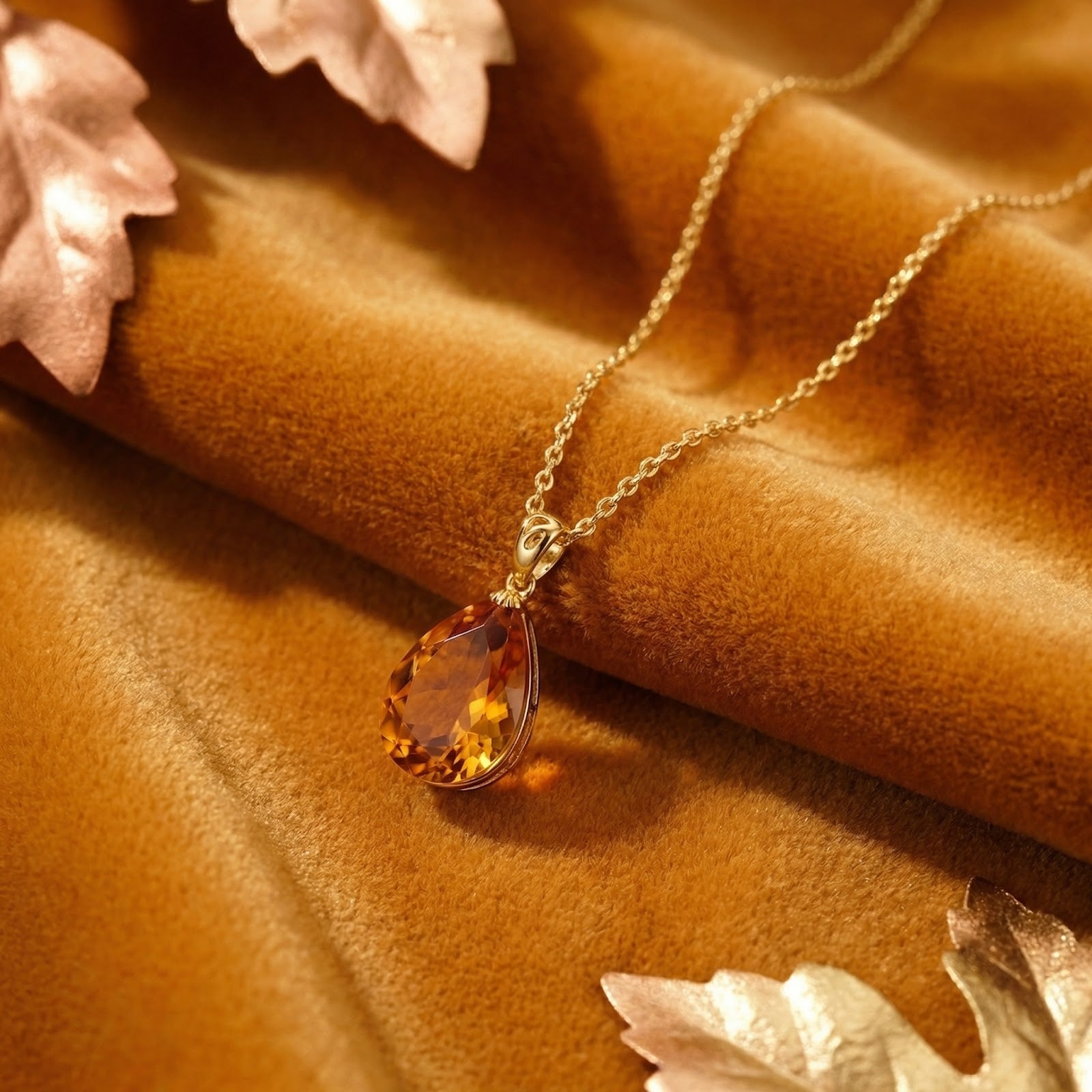 Lifestyle view of the 18K gold vermeil teardrop simulated topaz necklace styled with metallic autumn leaves.