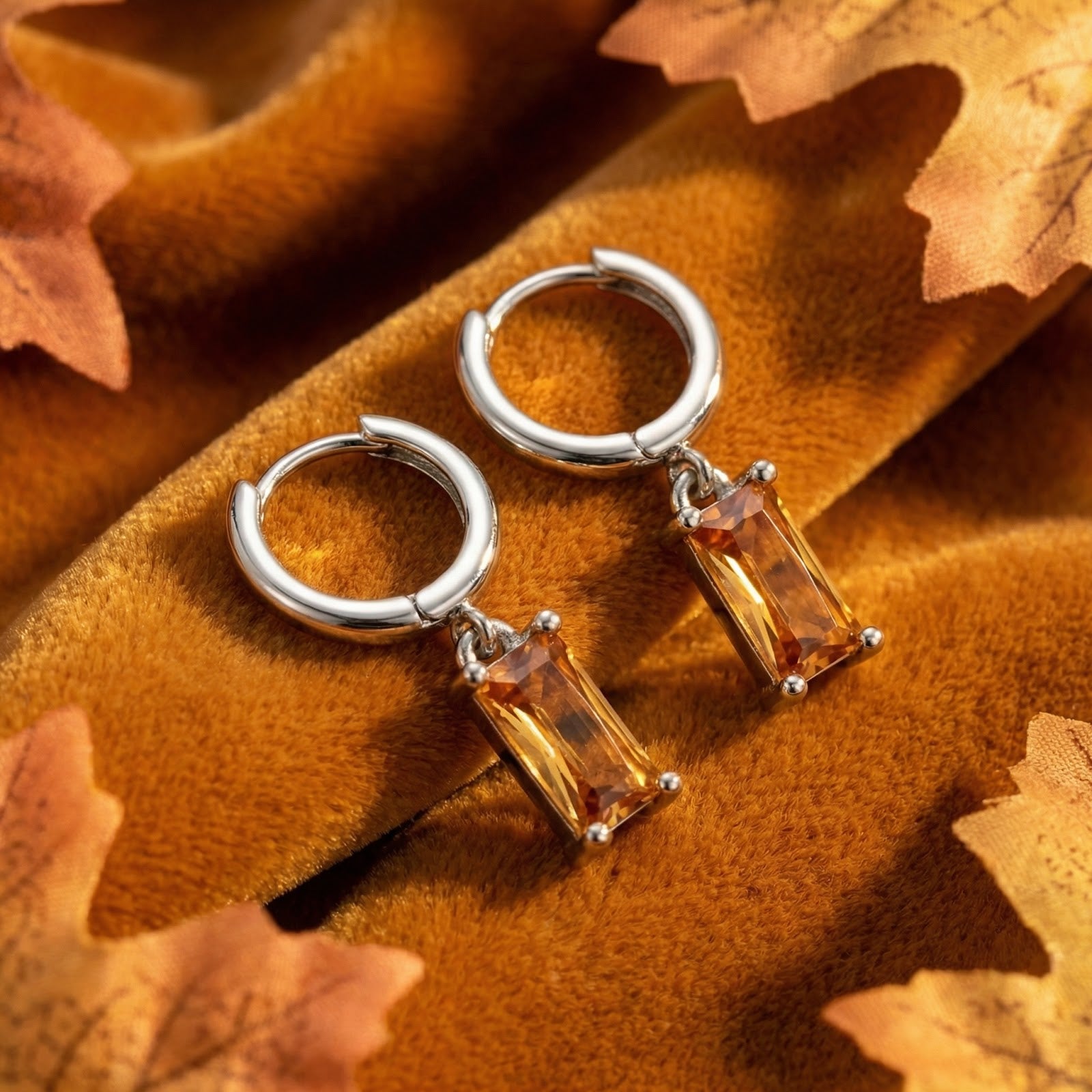 Silver-toned drop earrings with emerald-cut honey topaz stones on a brown velvet surface with fall leaves.