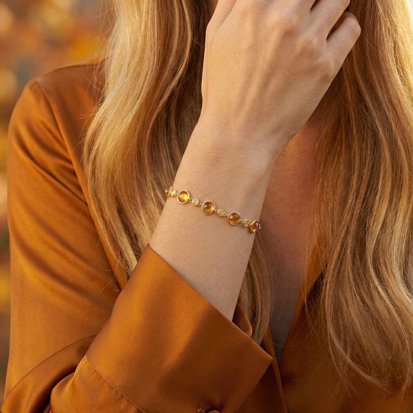 18K gold vermeil station bracelet with round simulated topaz stones worn on a model's wrist in a silk shirt.