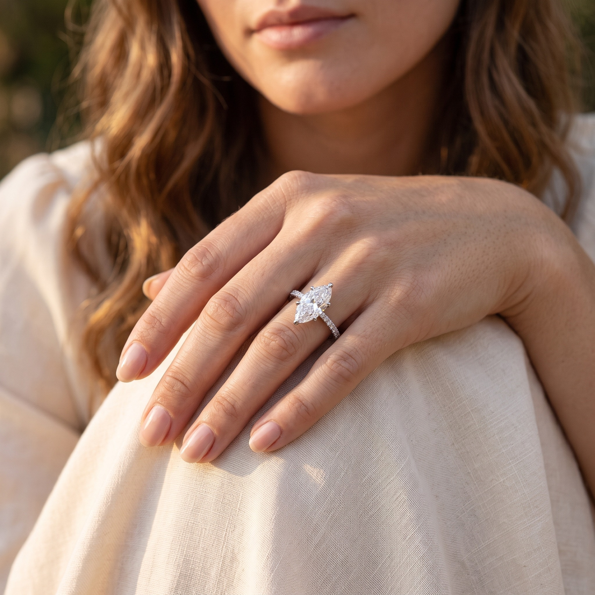 Silver marquise moissanite ring worn on a model's hand resting on her knee.