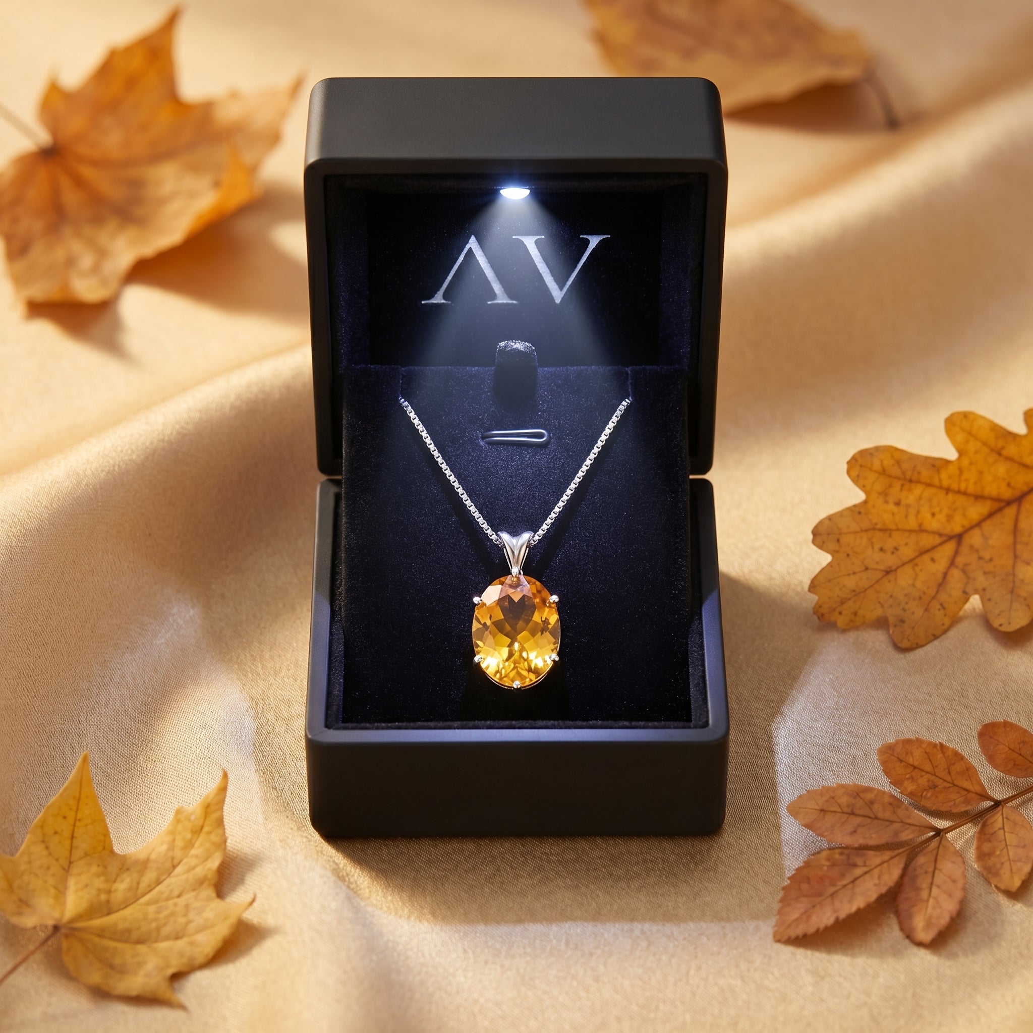 Oval natural citrine necklace presented in a lighted black jewelry gift box, surrounded by autumn leaves.