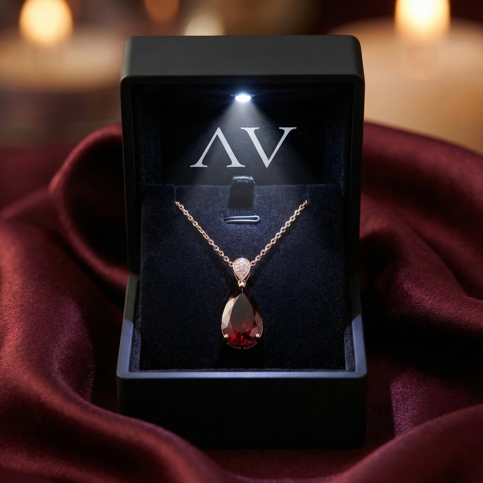 The Calista pear-cut garnet necklace presented in a premium black lighted gift box on burgundy silk fabric.