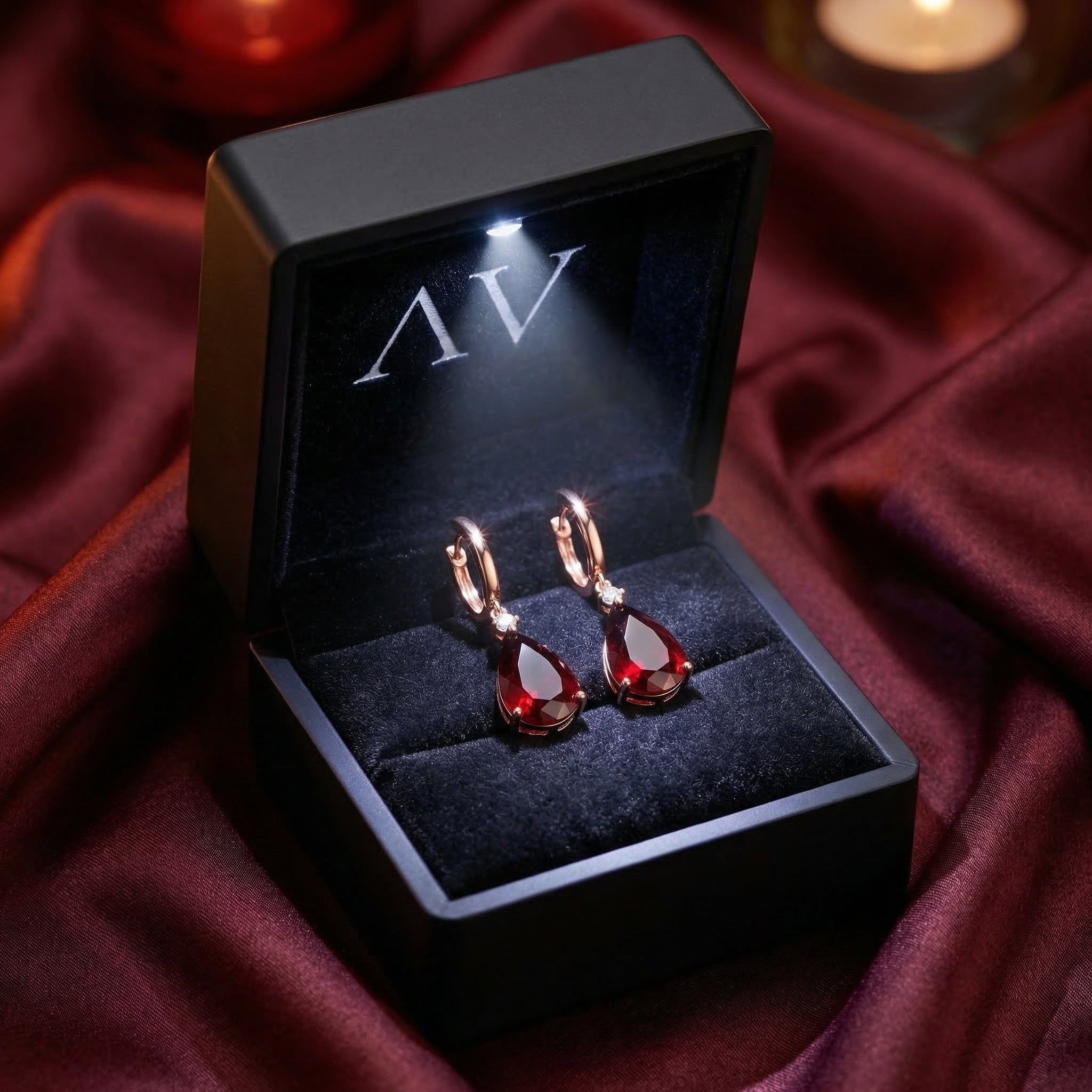 18K rose gold pear-cut garnet drop earrings inside a black lighted jewelry box on burgundy fabric.