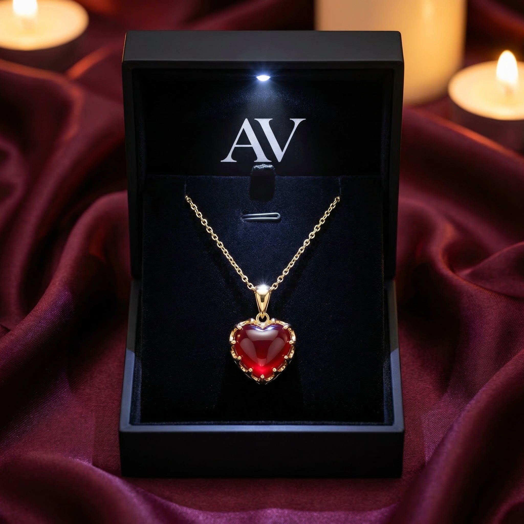 Heart-cut red garnet gold necklace presented in a black lighted gift box on a burgundy silk background.