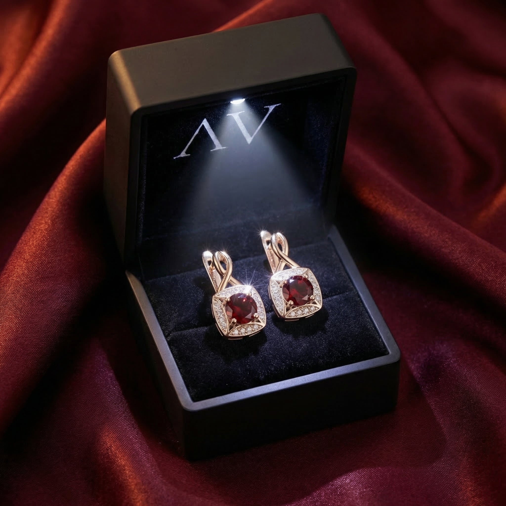 Round-cut garnet and sterling silver drop earrings presented in a lighted black jewelry gift box.