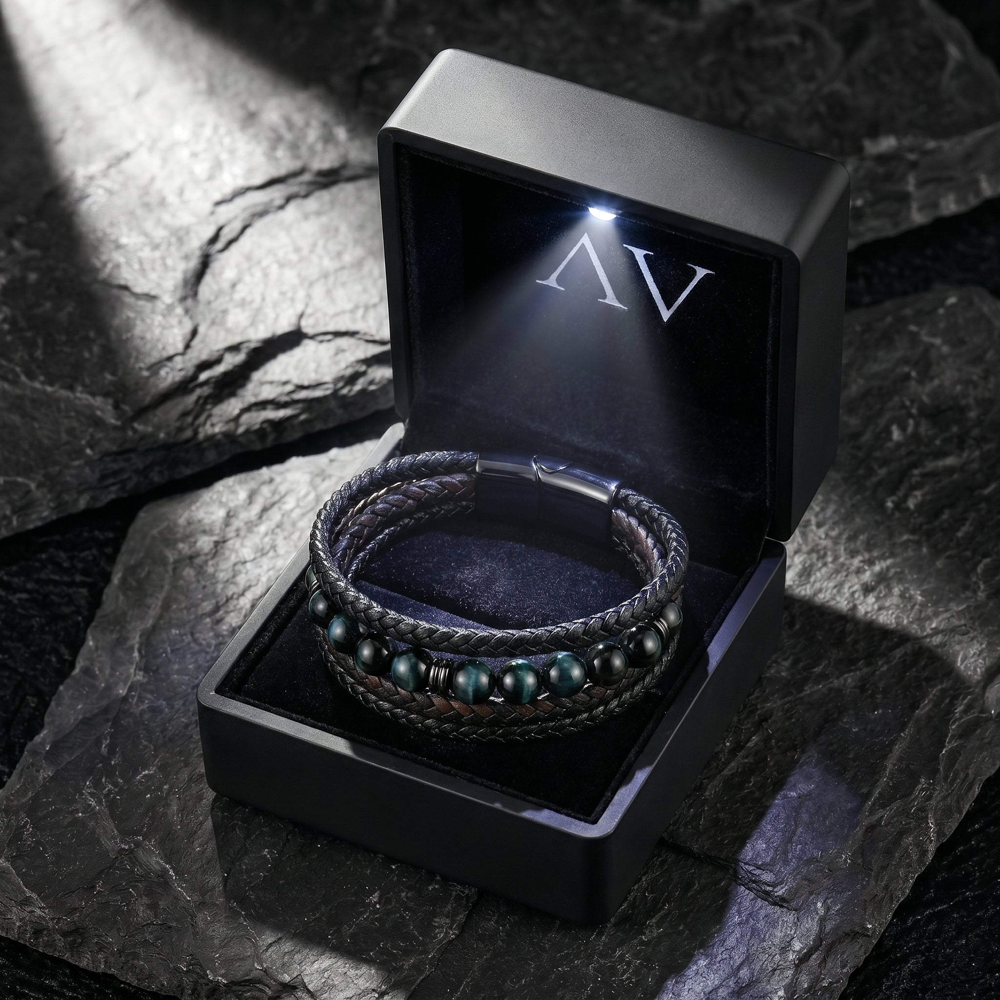 Multi-layered braided leather bracelet presented in a black illuminated gift box on a stone surface.