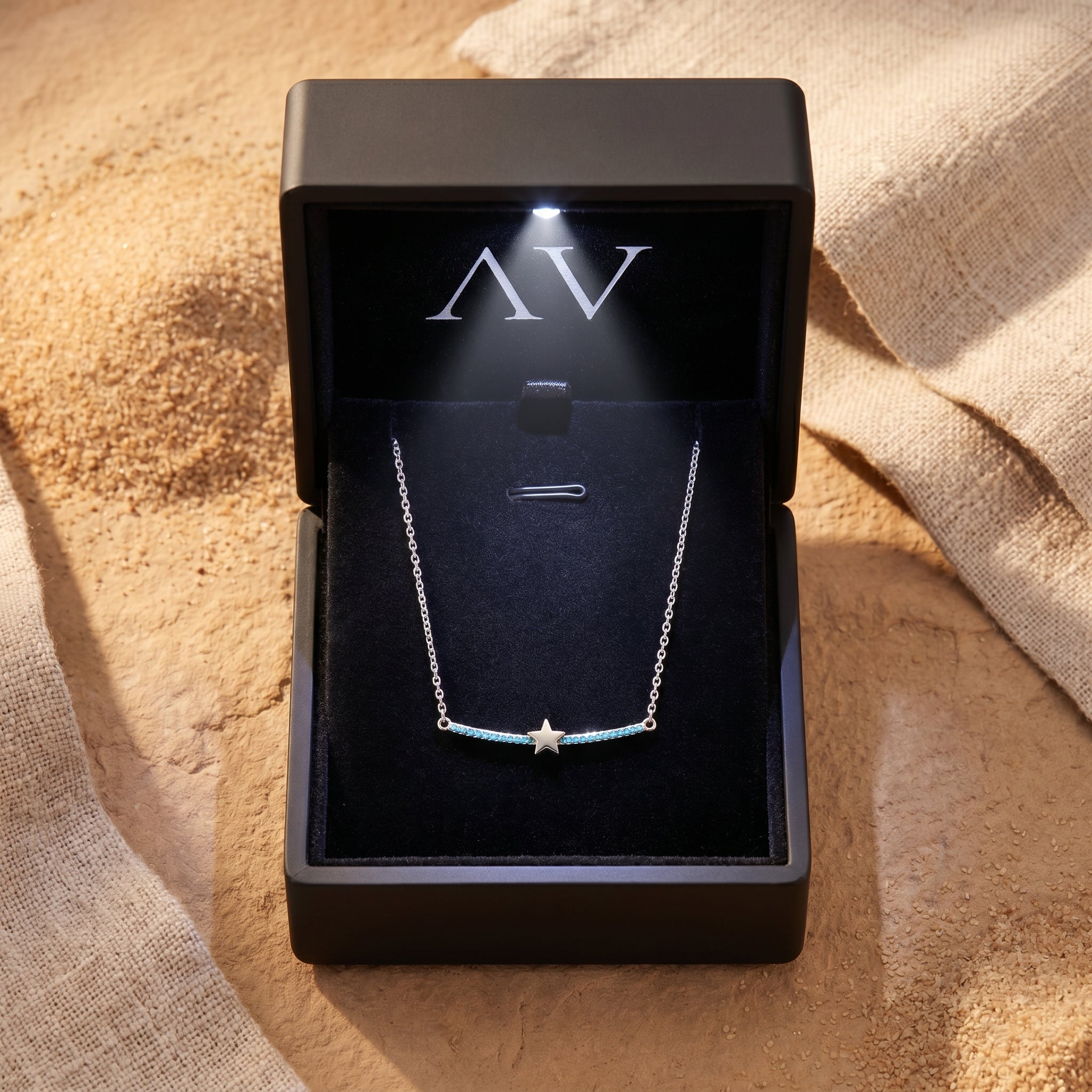 Silver Phoenix Star turquoise necklace inside a premium black lighted jewelry gift box on a sandy surface.