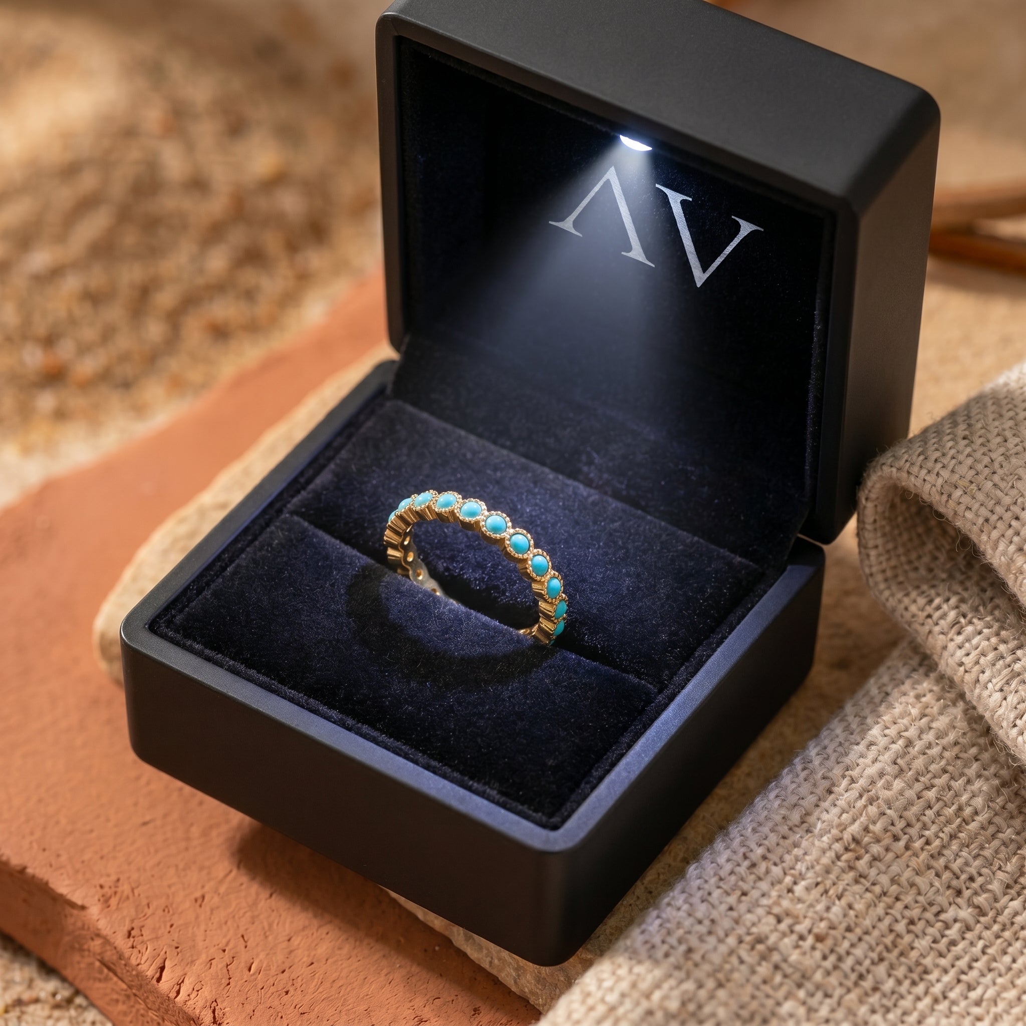 Gold Zia turquoise eternity ring inside a black LED-lighted jewelry gift box on a rustic background.