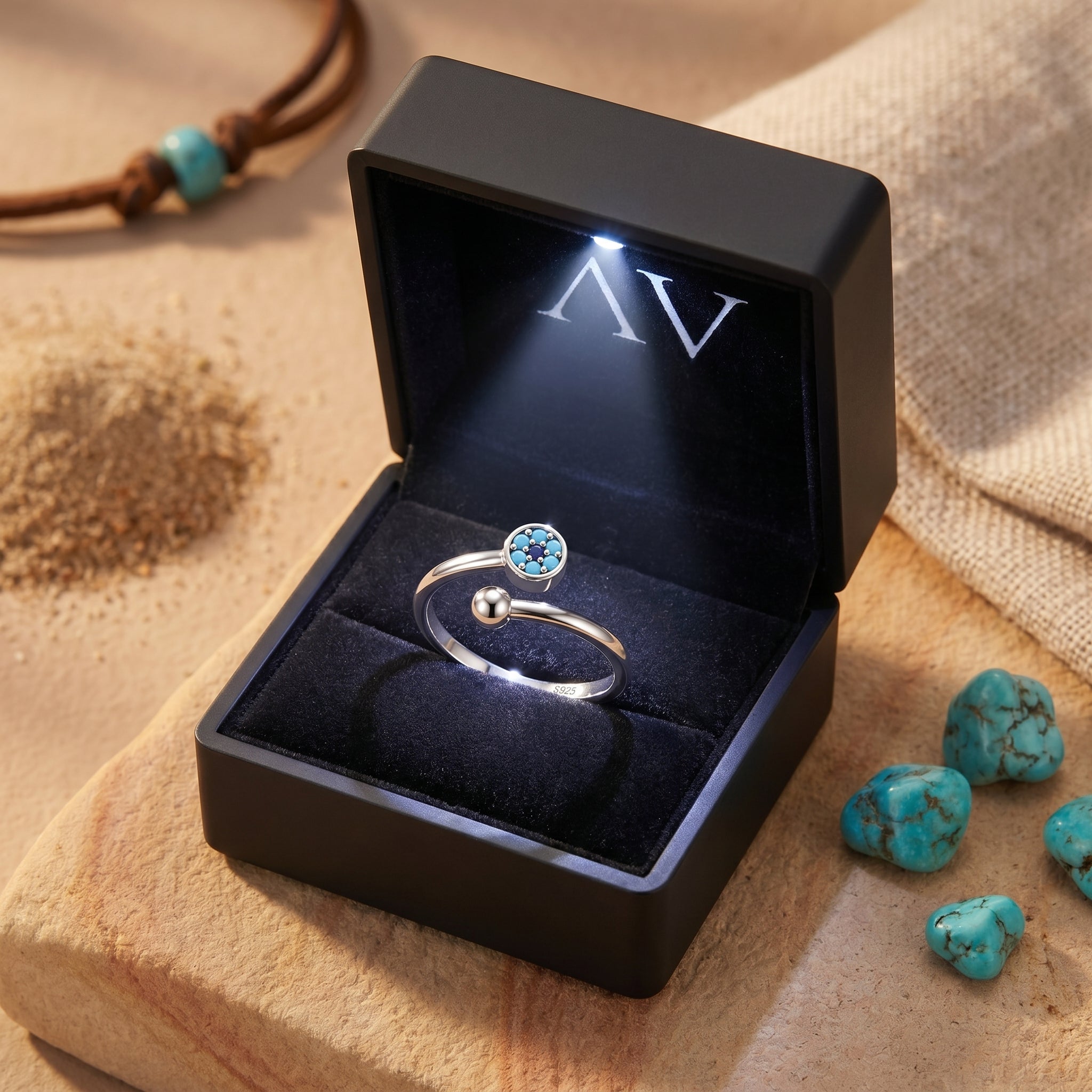 Silver turquoise bypass ring presented in a black LED-lit gift box on a desert-themed surface.