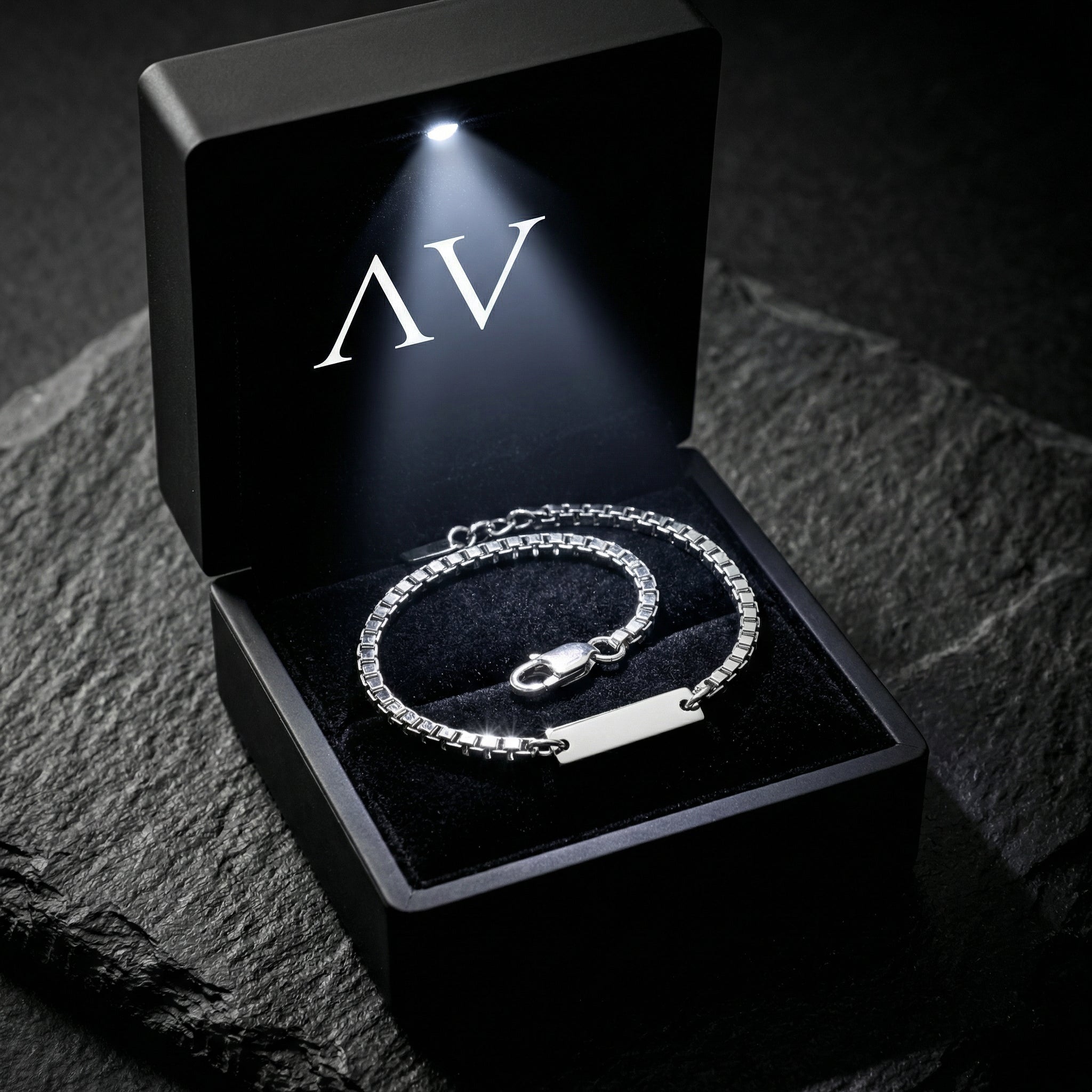 Silver stainless steel box chain bracelet presented in a black LED-lit jewelry gift box on stone.