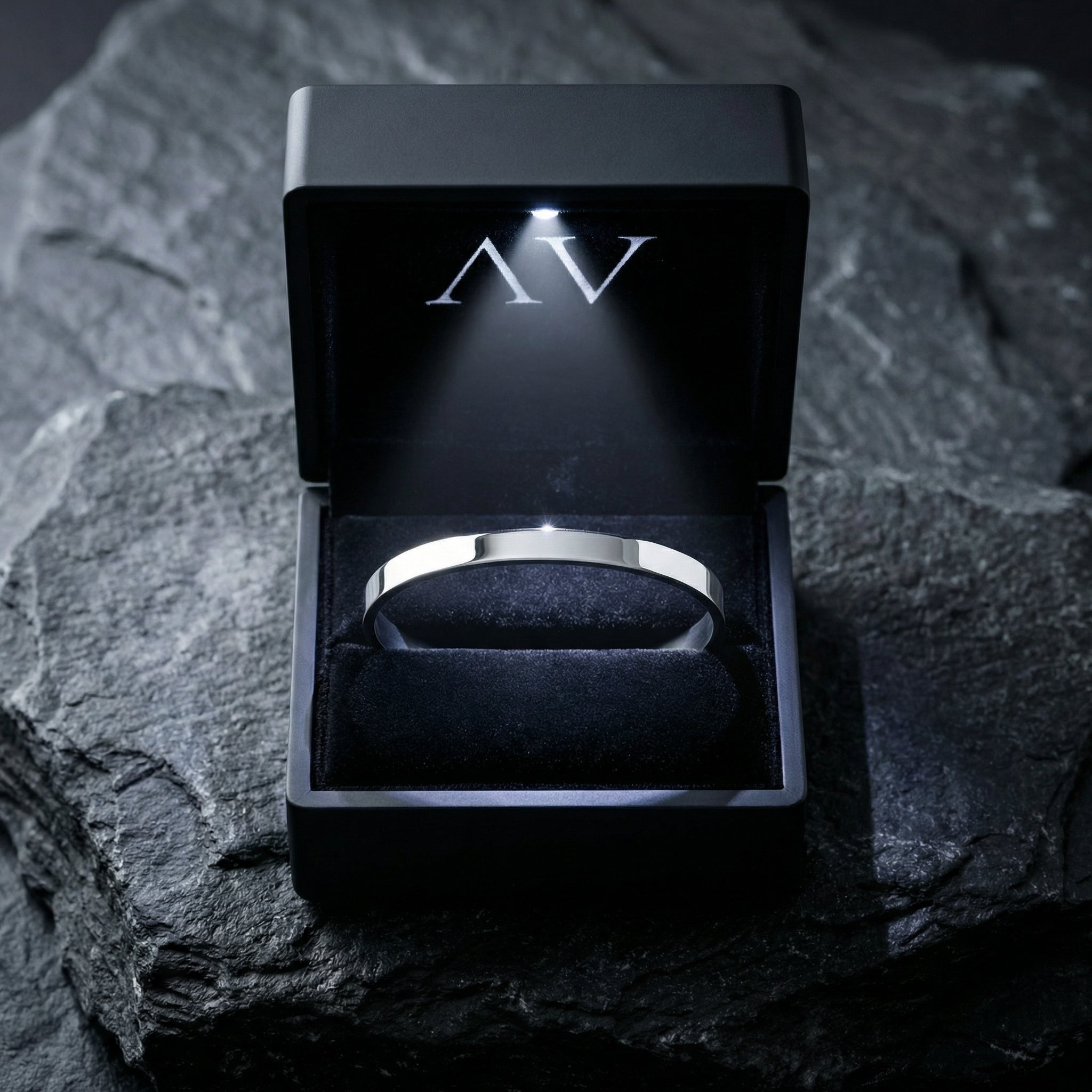 Silver stainless steel cuff bracelet displayed inside a black LED-lit jewelry gift box on a stone surface.
