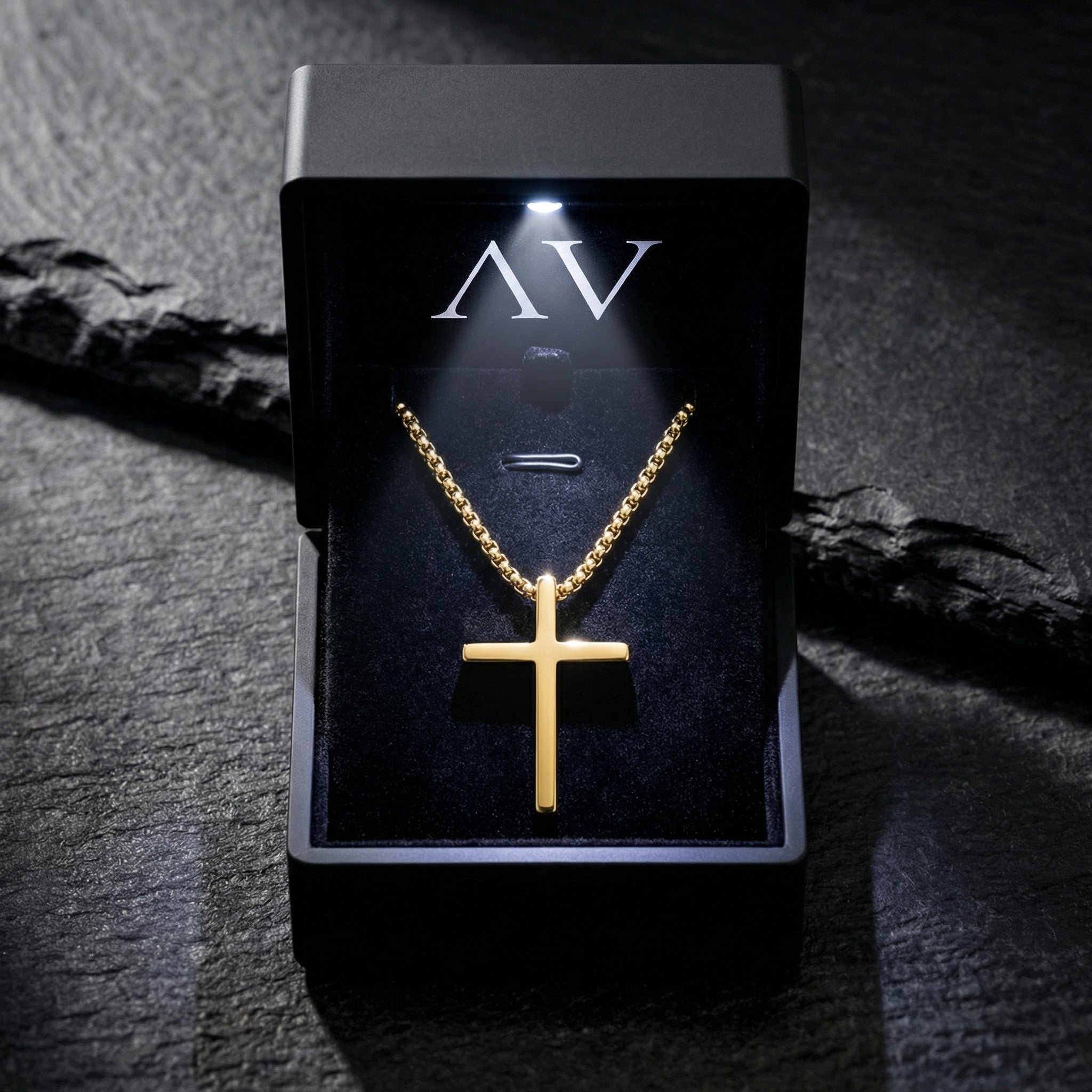 Gold tone stainless steel Devotion Cross necklace inside a black LED-lit gift box on a stone surface.