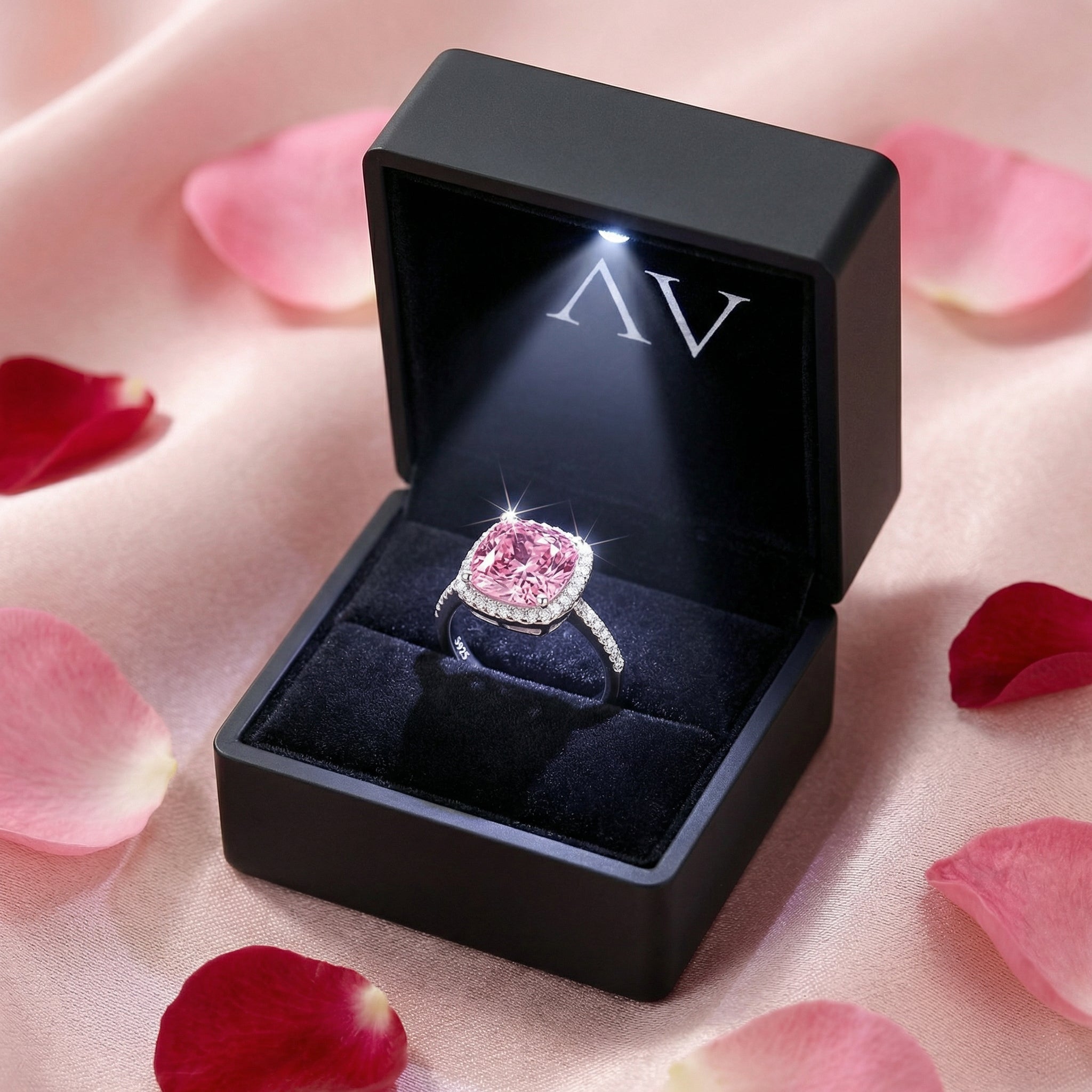 Cushion cut pink tourmaline sterling silver halo ring in a black LED-lighted jewelry box with rose petals.