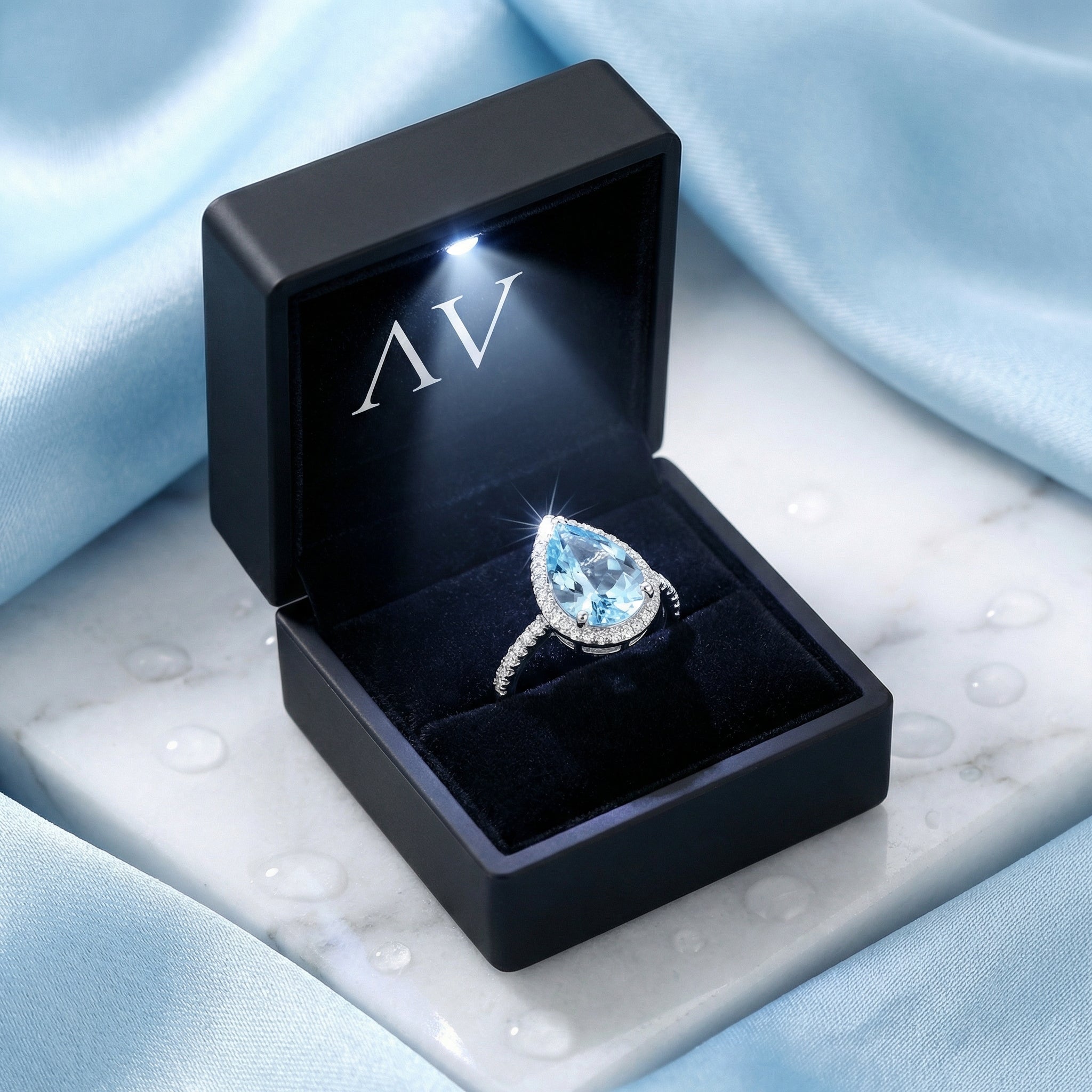 Pear cut simulated aquamarine ring presented in a black light-up jewelry box on a marble surface.