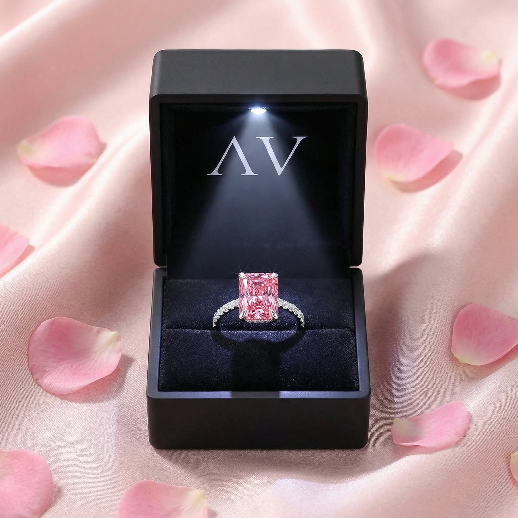 Radiant cut pink tourmaline silver ring in a black lighted jewelry box with rose petals.