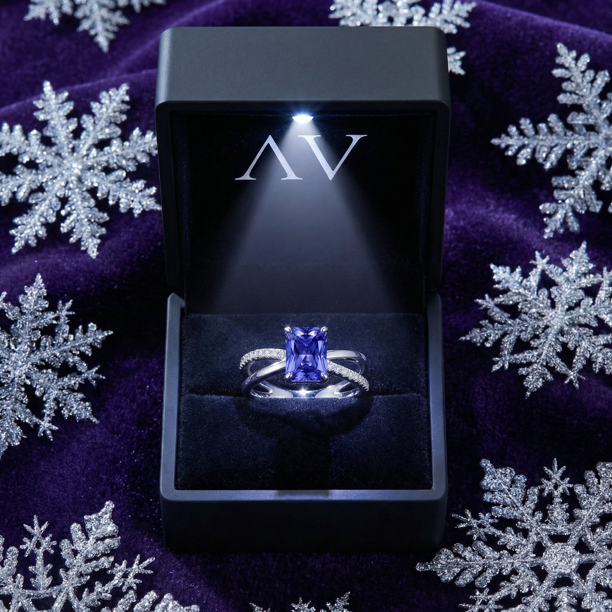 Radiant-cut simulated tanzanite ring in a lighted black jewelry box on a purple snowflake background.