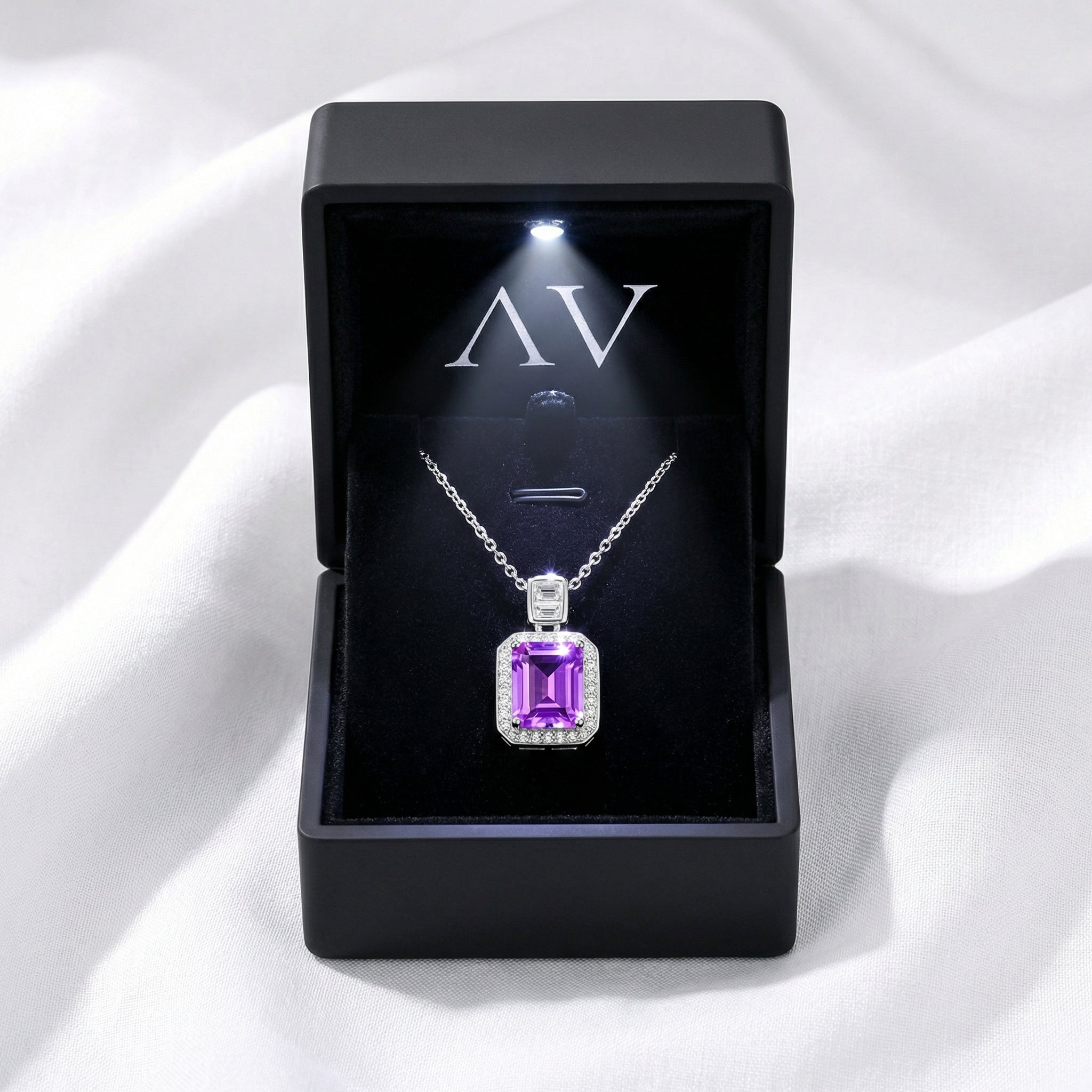 Purple simulated amethyst pendant necklace in a lighted black jewelry gift box on white fabric.