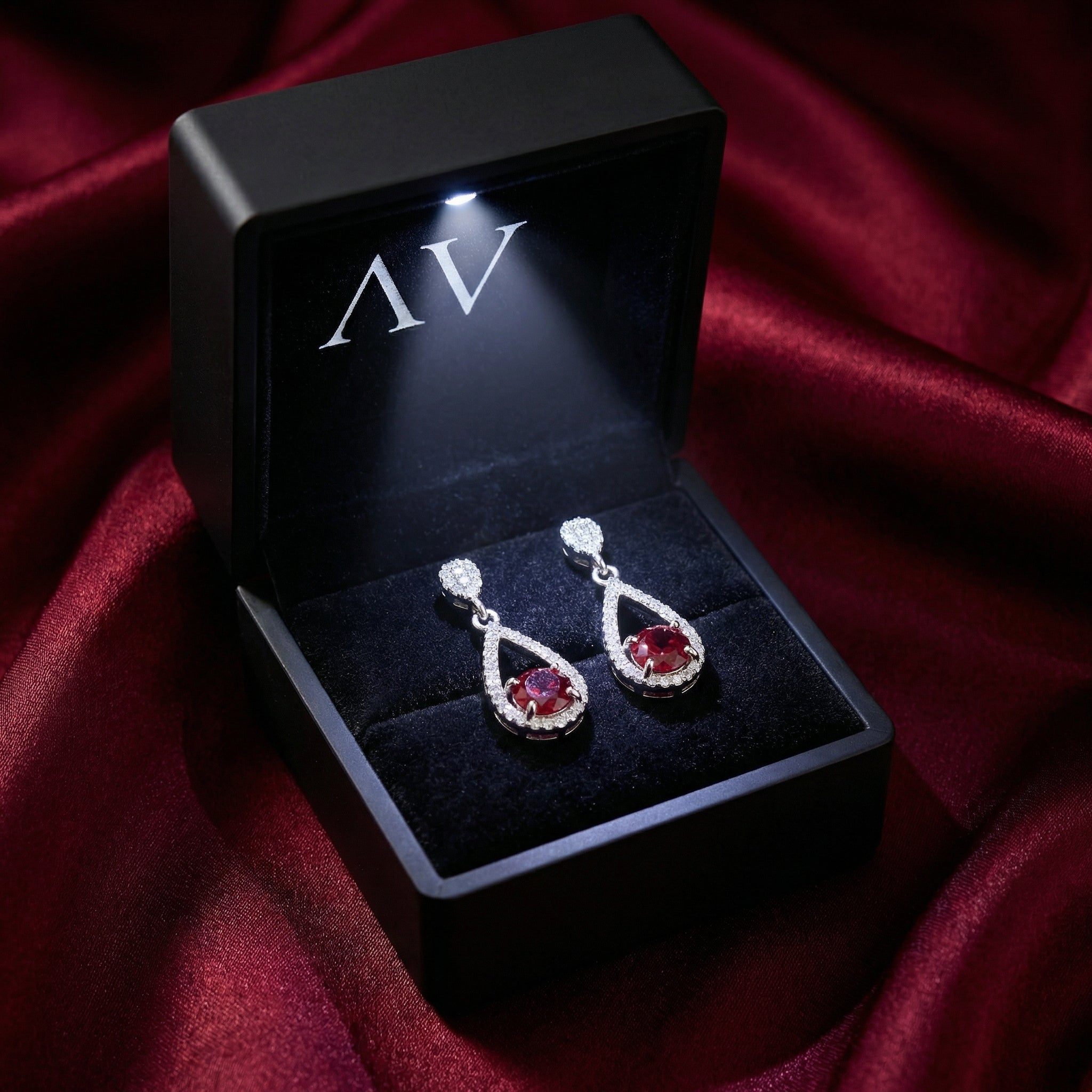 Pair of S925 sterling silver simulated ruby drop earrings in a lighted black presentation gift box.