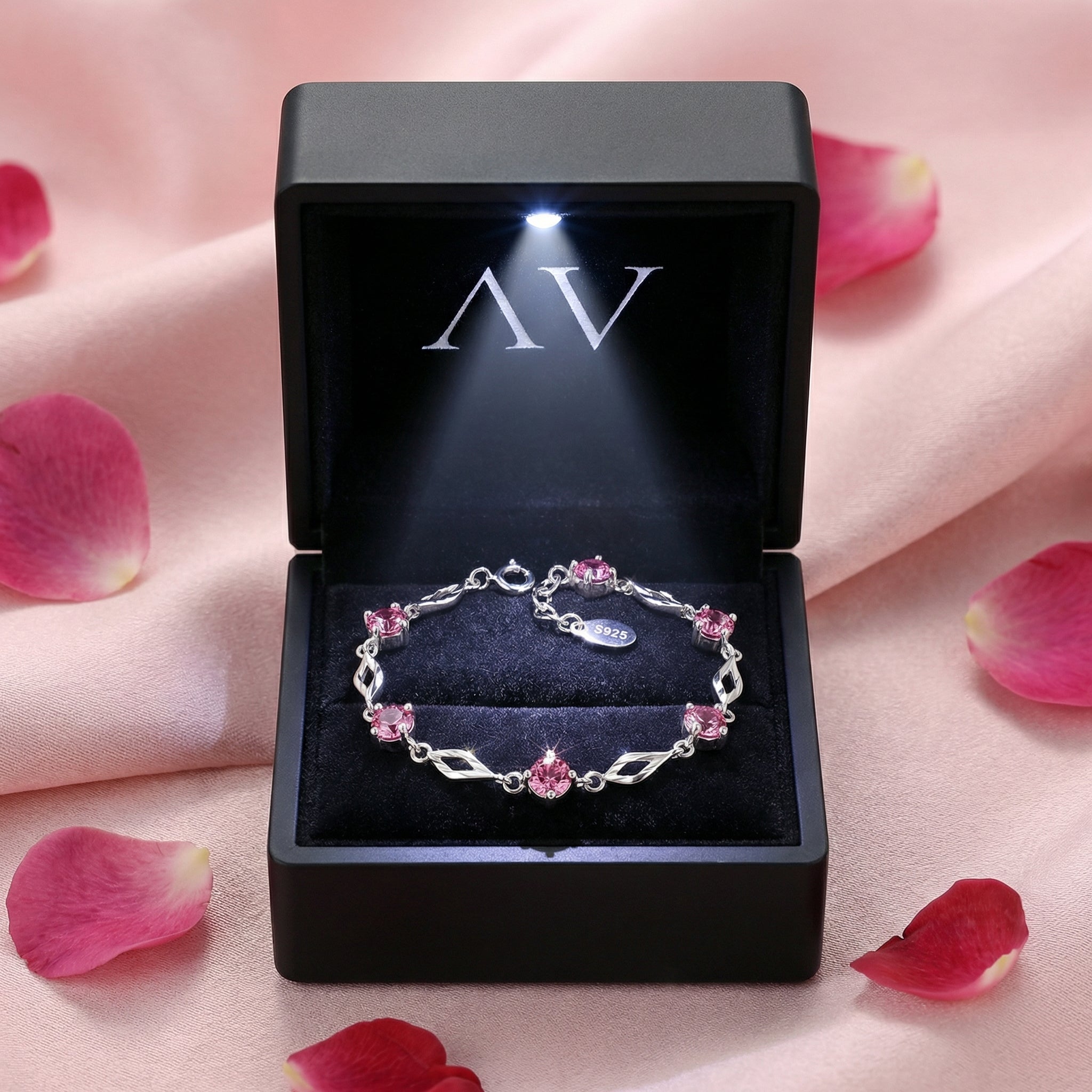 Pink tourmaline sterling silver station bracelet in a black LED-lit gift box surrounded by rose petals.
