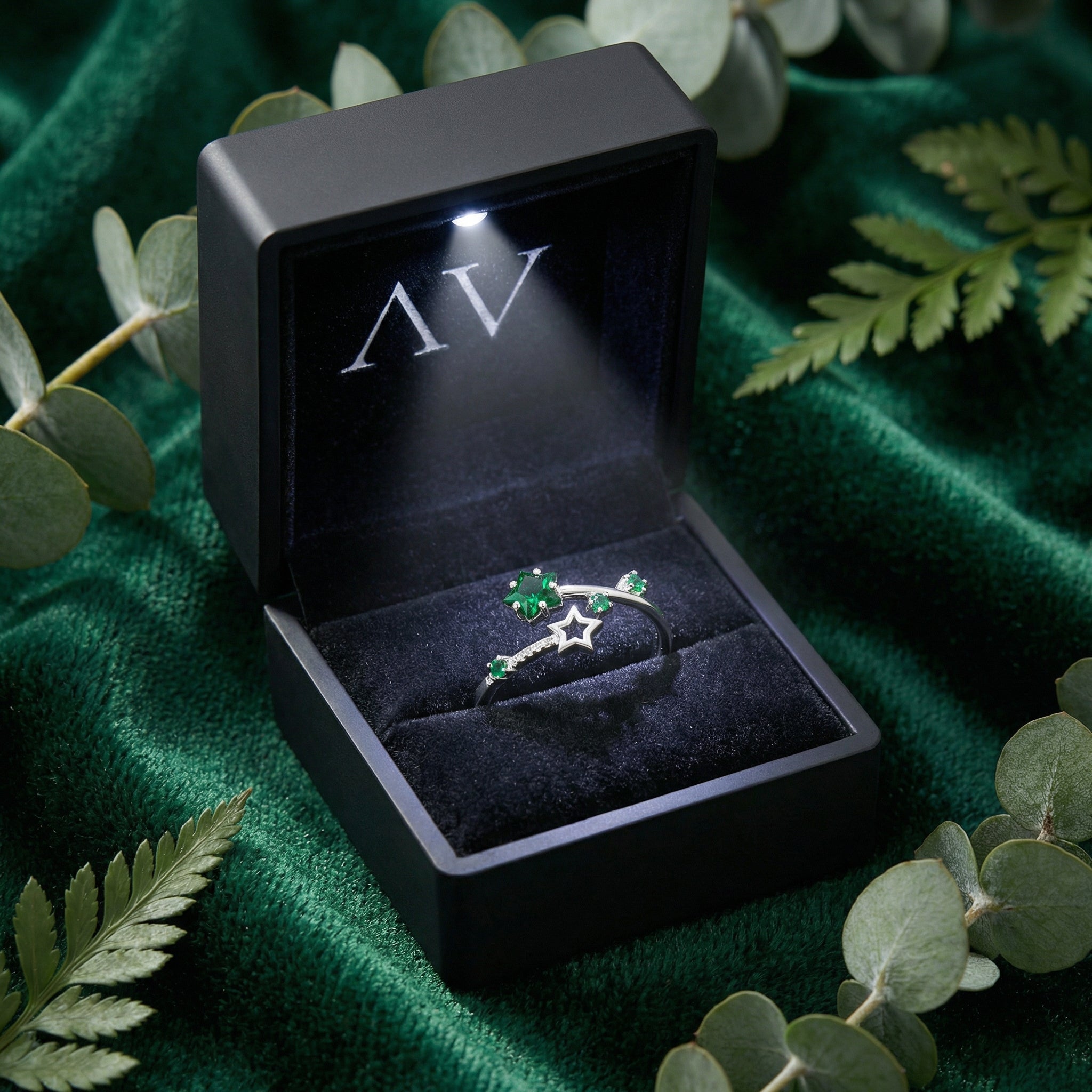 Silver Vega Star ring with green emeralds inside a black LED-lit jewelry box on green velvet.