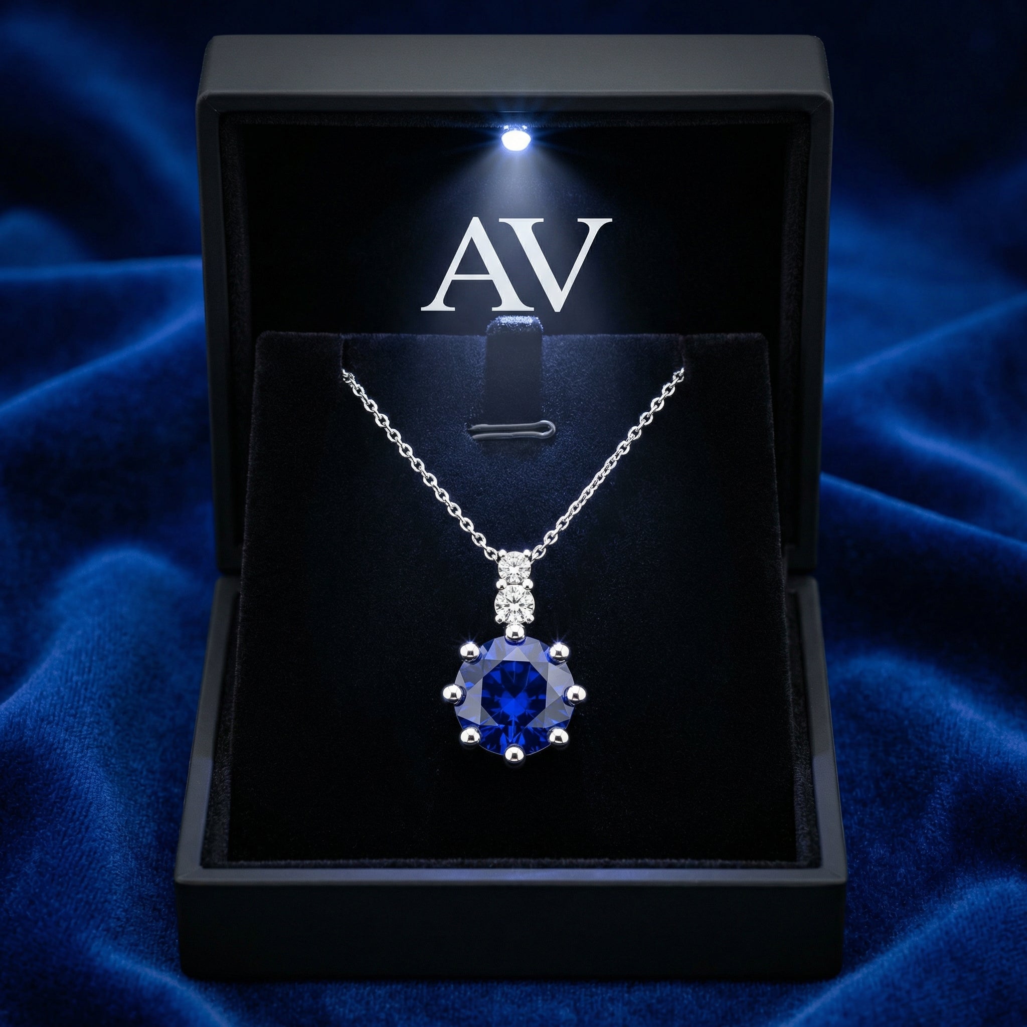 Sterling silver blue sapphire pendant presented in a black lighted gift box on blue velvet.