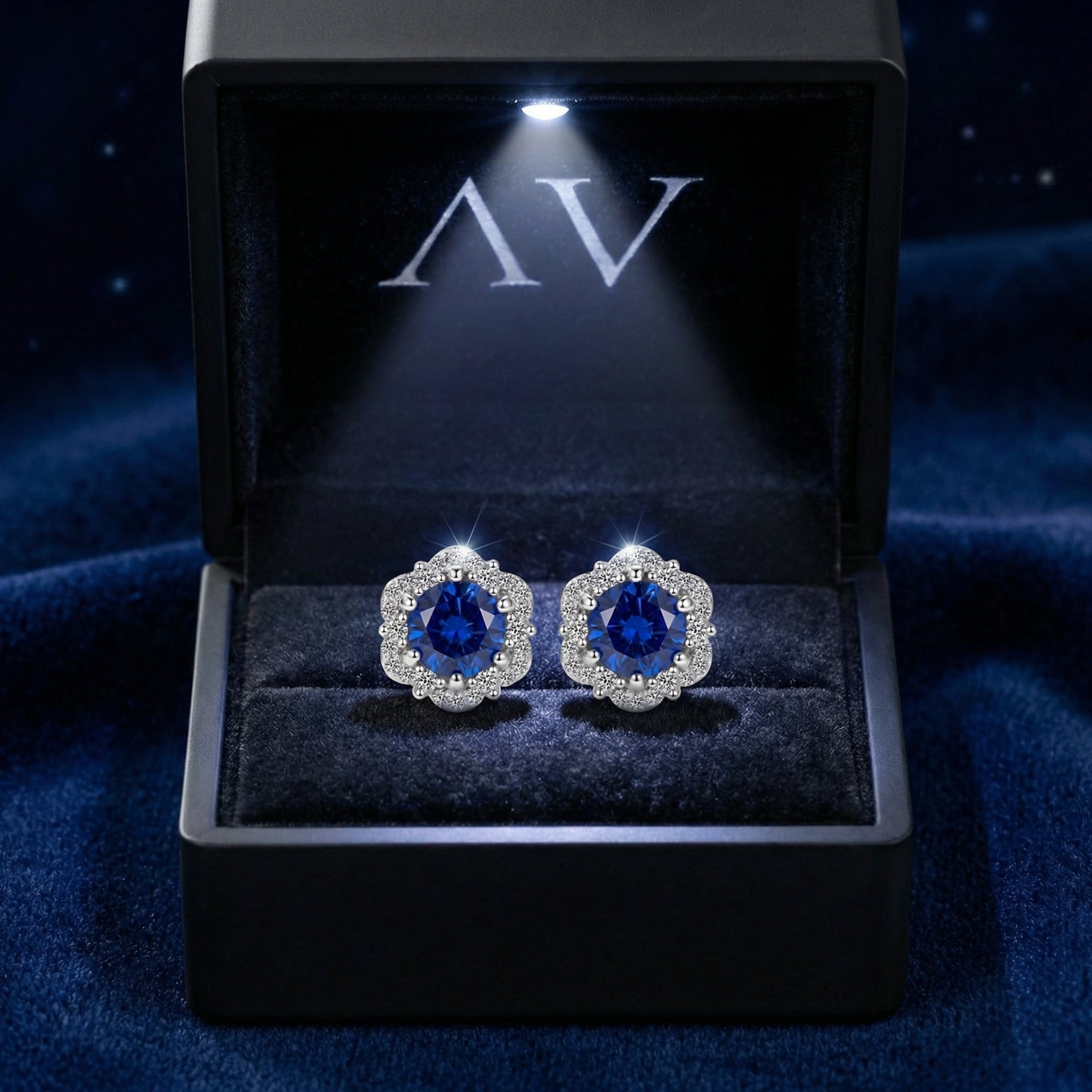 Simulated sapphire halo stud earrings presented in a lighted black gift box on a blue velvet surface.