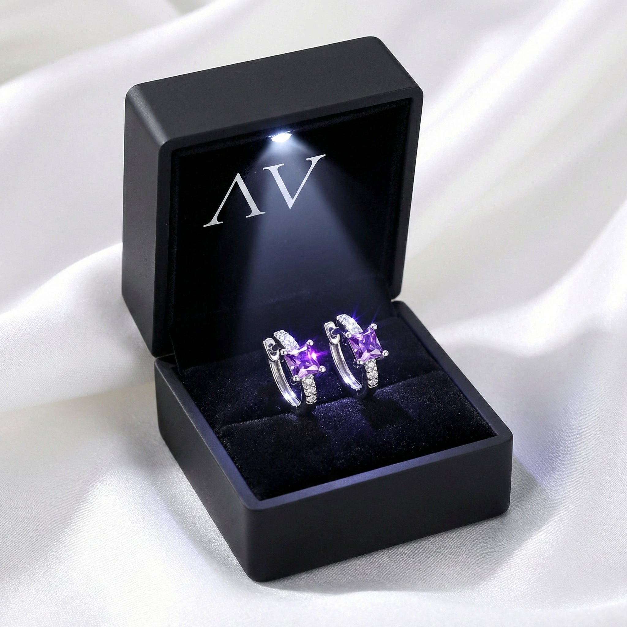 Sterling silver simulated amethyst huggie earrings in a black LED-lit jewelry presentation box.