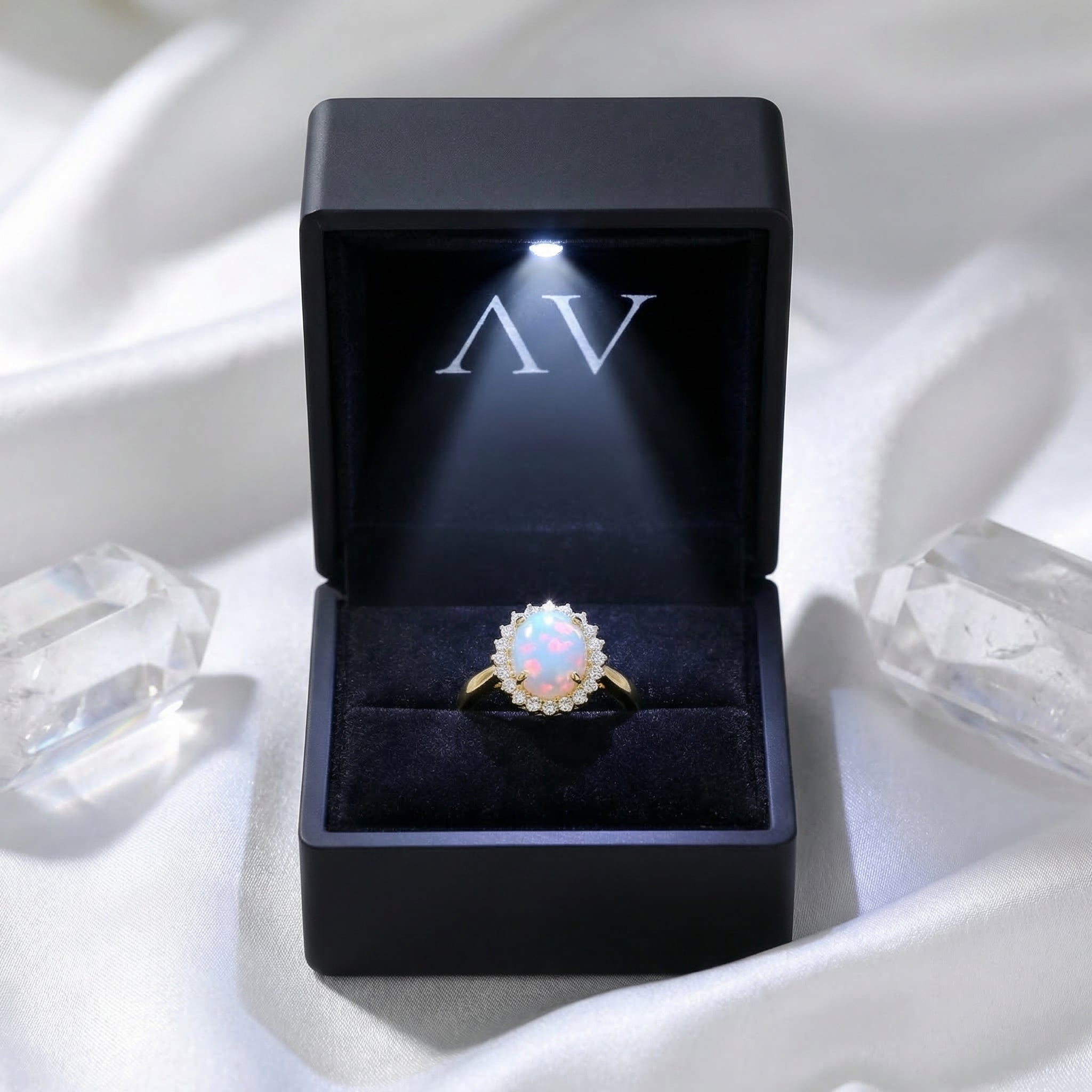Gold oval opal halo ring presented in a black LED-lighted jewelry box on white silk with crystals.