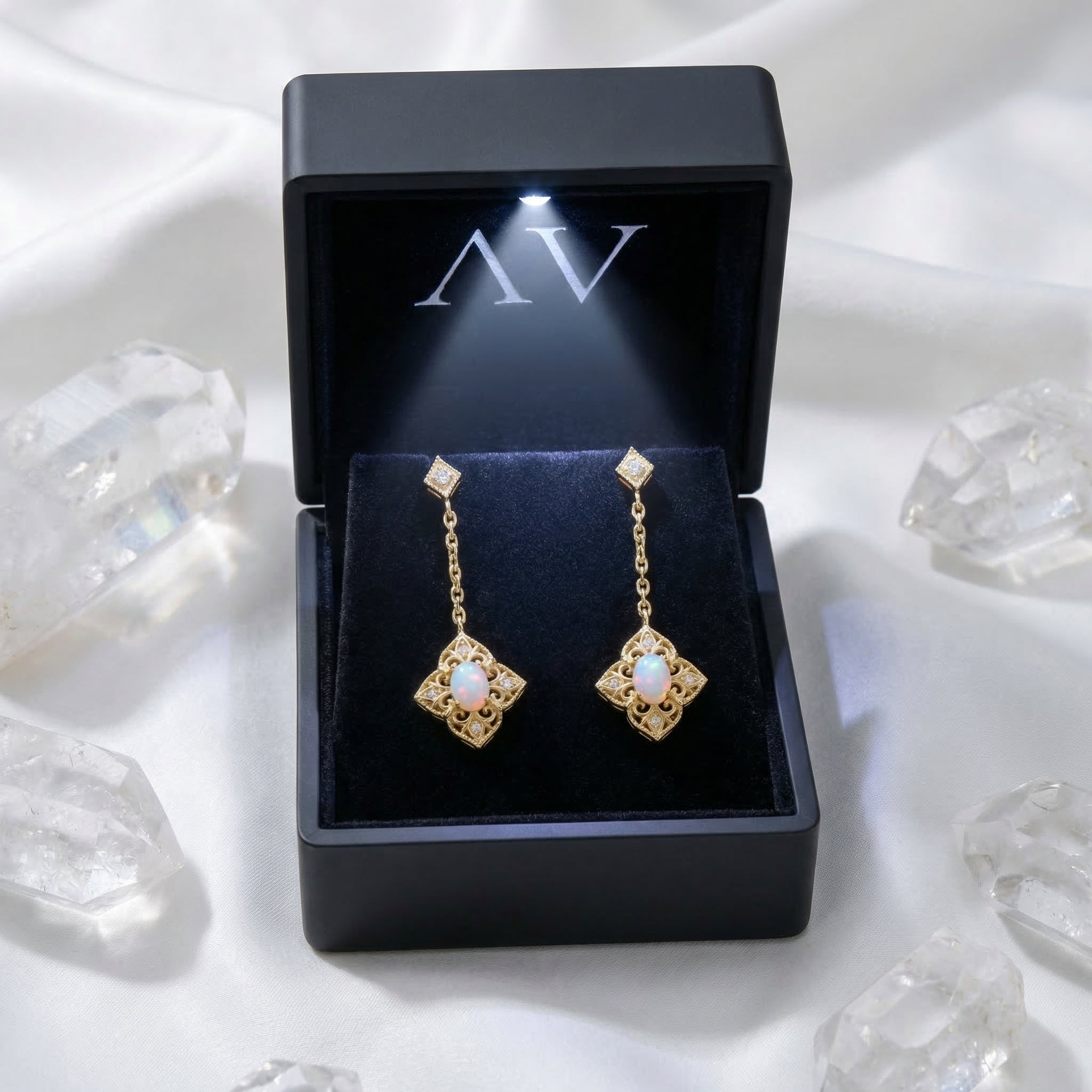 Gold-tone white opal filigree drop earrings inside a black illuminated jewelry presentation box.