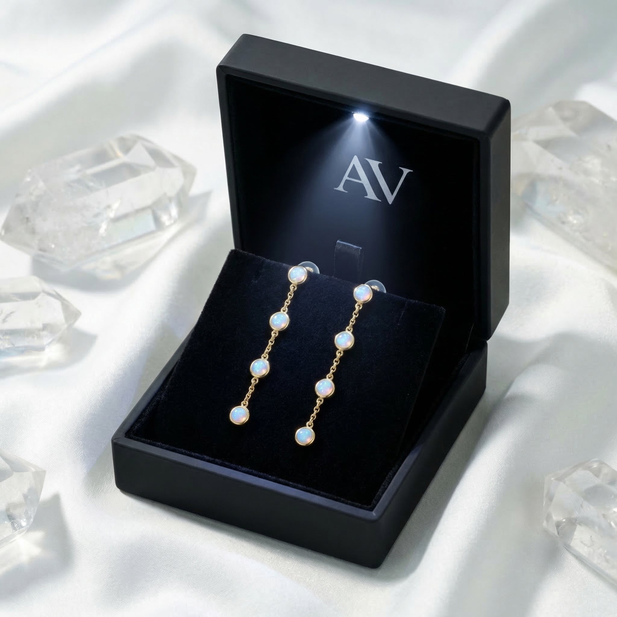 Gold and white opal drop earrings presented in a black illuminated jewelry gift box with AV branding.