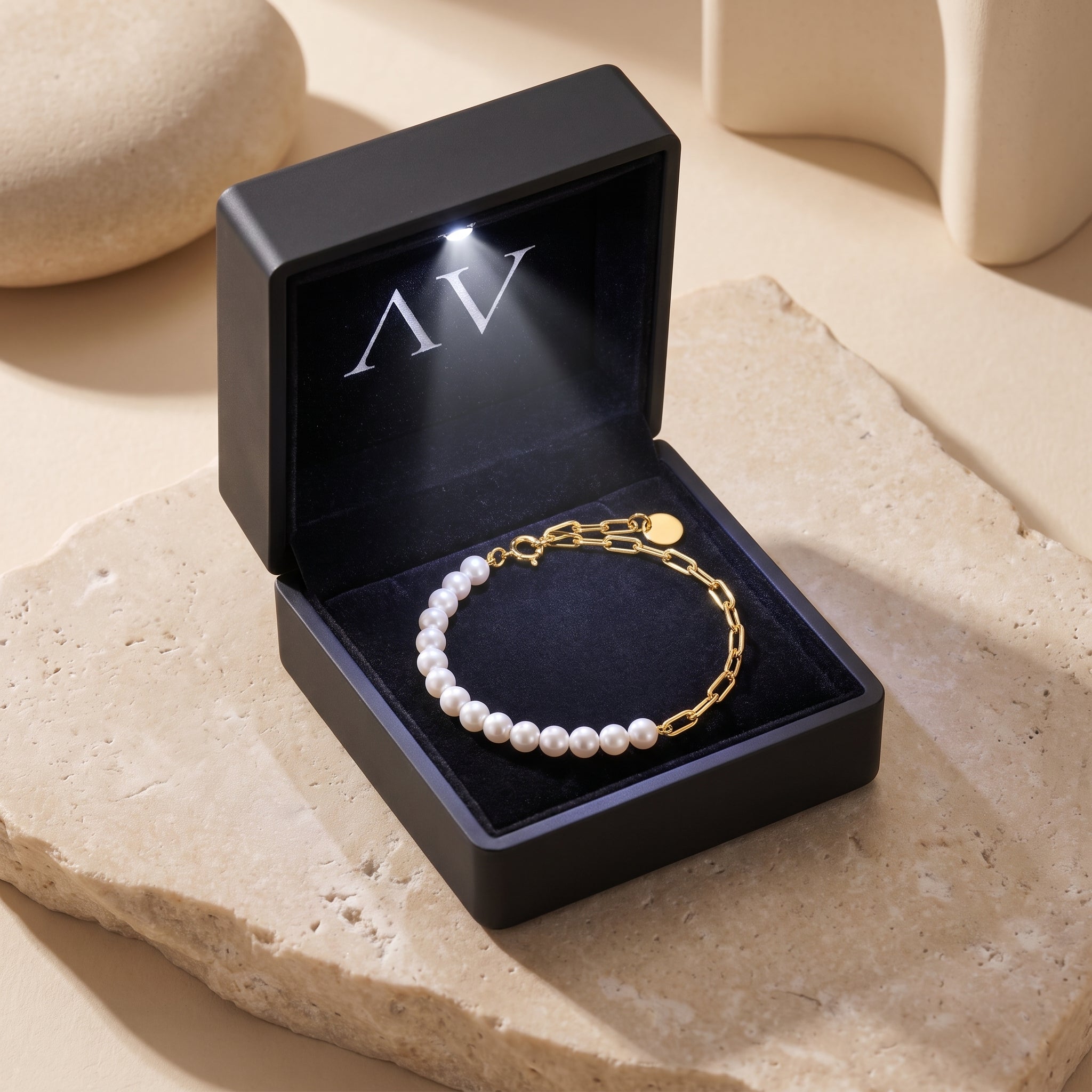 Gold and pearl bracelet presented in a black illuminated jewelry gift box on a stone base.
