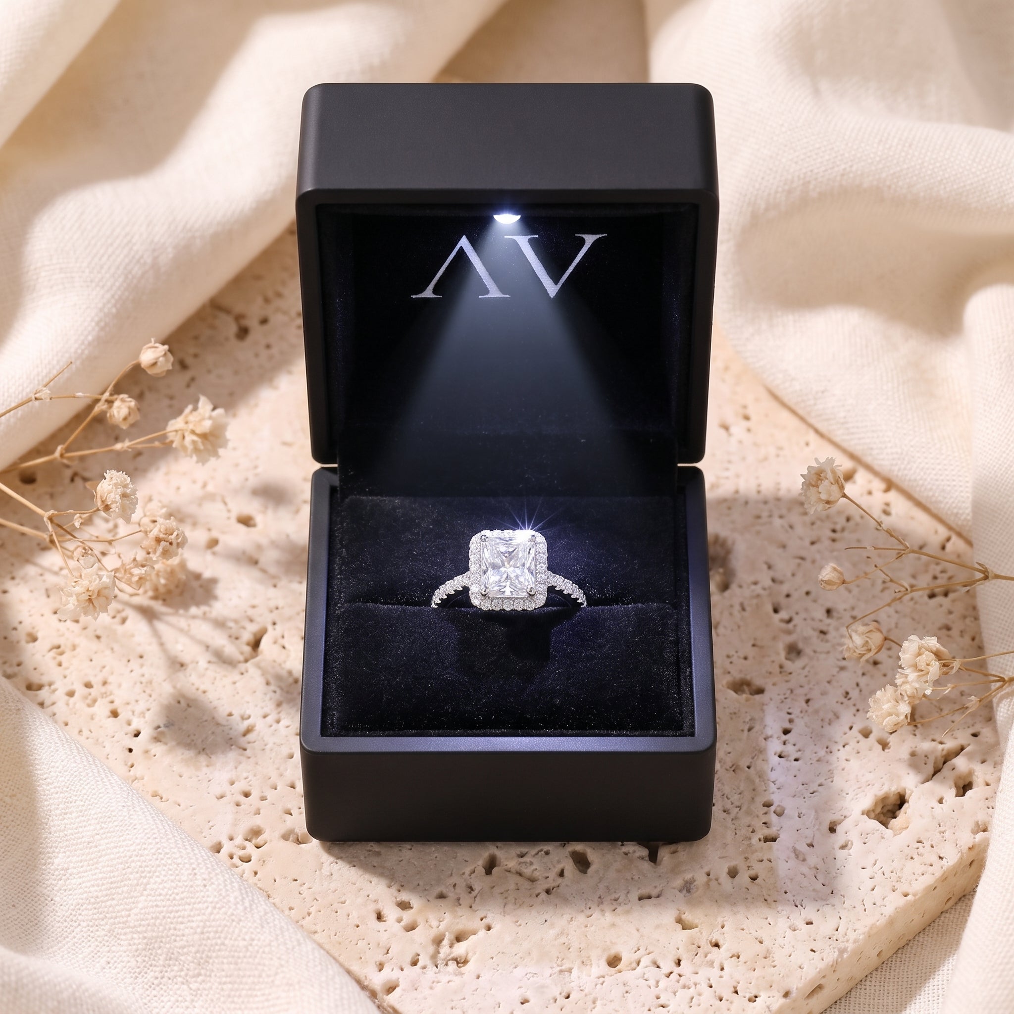 Radiant-cut cubic zirconia halo silver ring inside a black lighted presentation box on a styled background.
