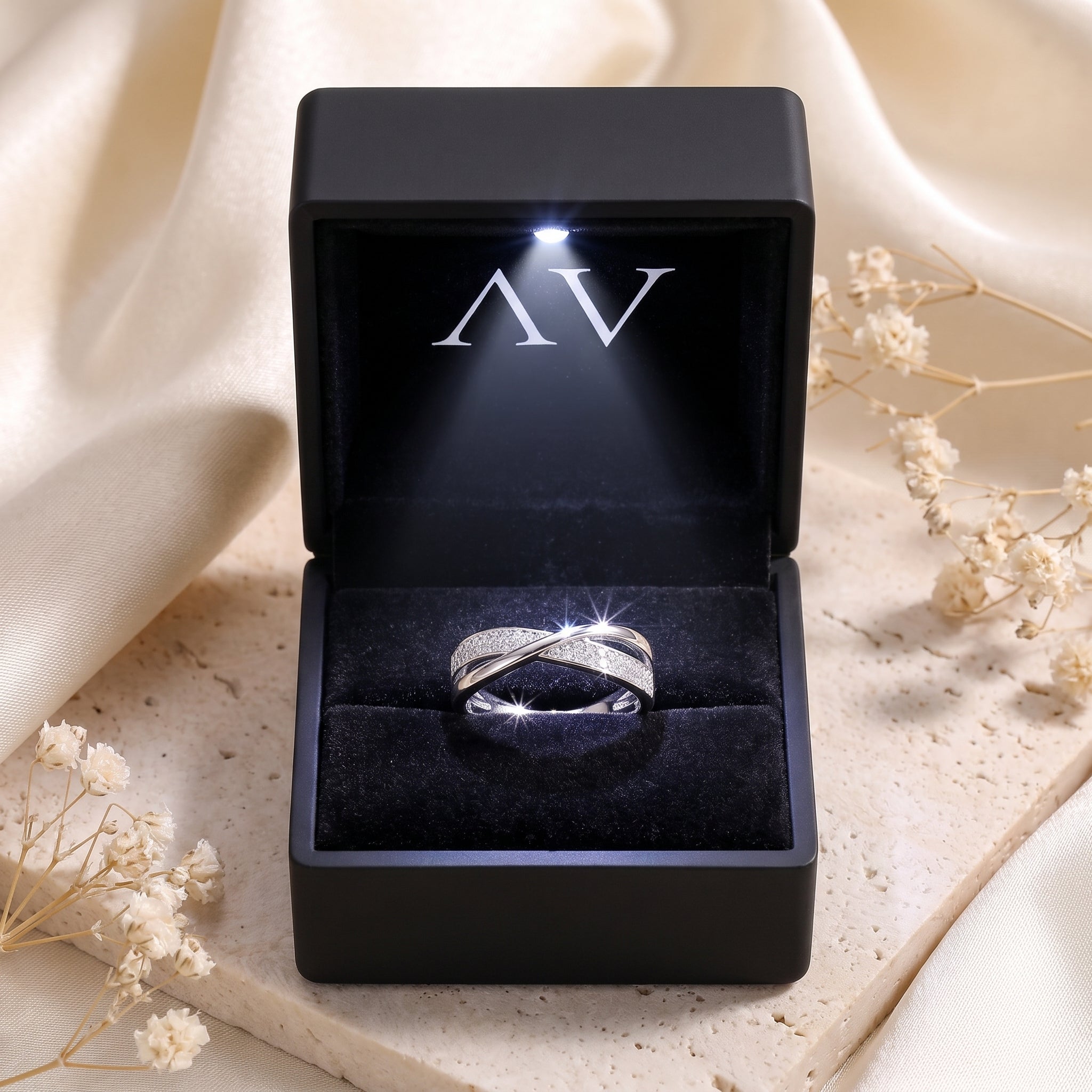 Silver crossover ring with pavé stones in a black lighted gift box.