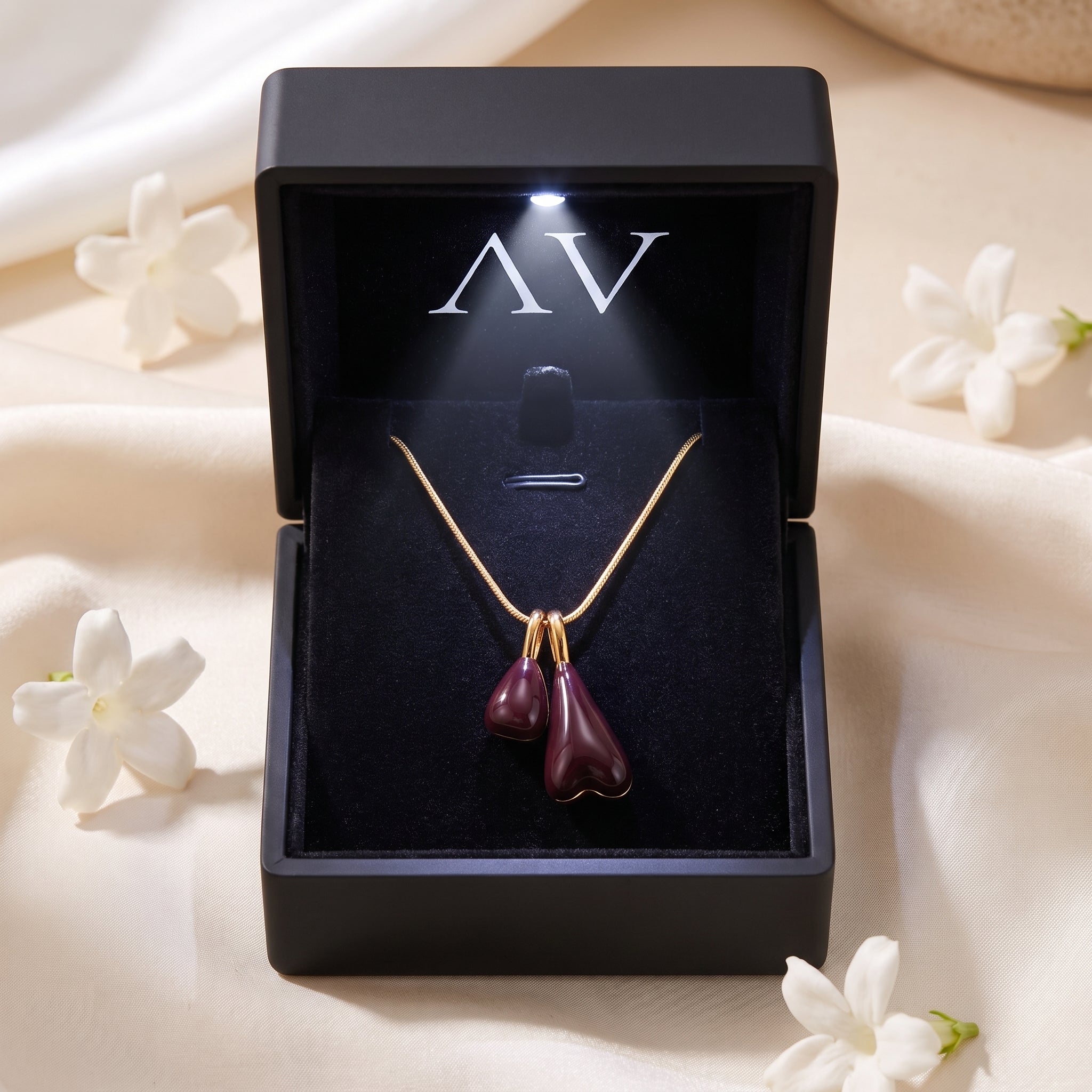 Marais gold pendant necklace with burgundy drops in a black lighted jewelry box with white flowers.
