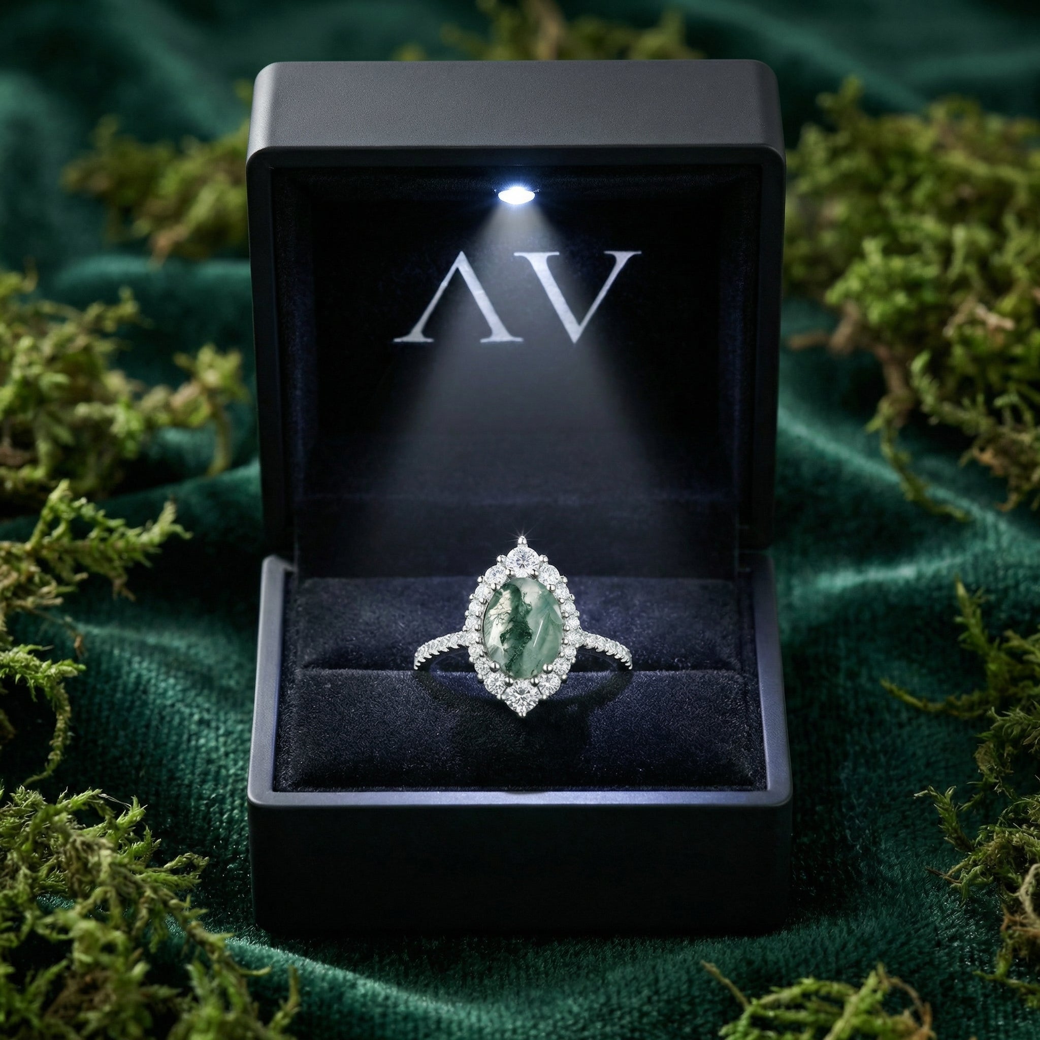 Oval moss agate sterling silver halo ring presented in a black lighted gift box on a green velvet surface.
