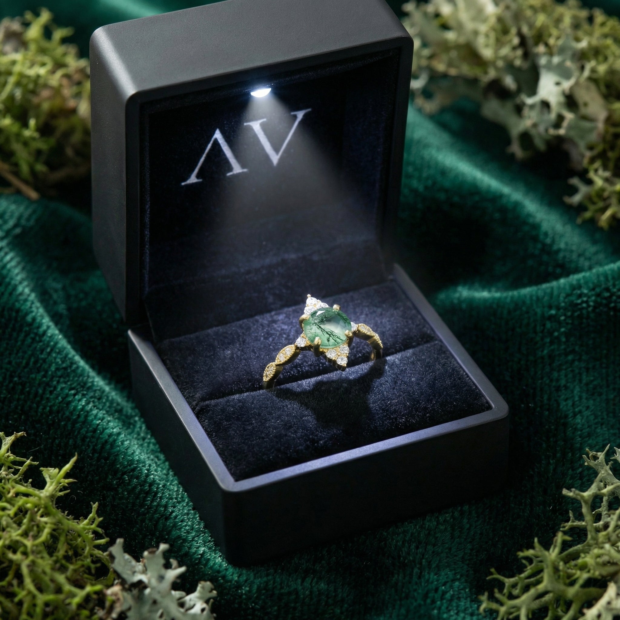 Gold moss agate sunburst ring inside a black lighted presentation box on a green velvet background.